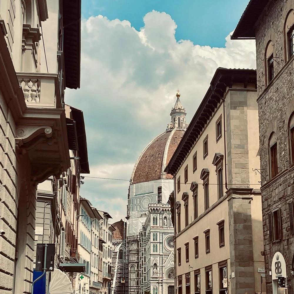 View of Florence, Italy, with the Florence Cathedral's dome (Duomo) towering over historic buildings on a cloudy day.