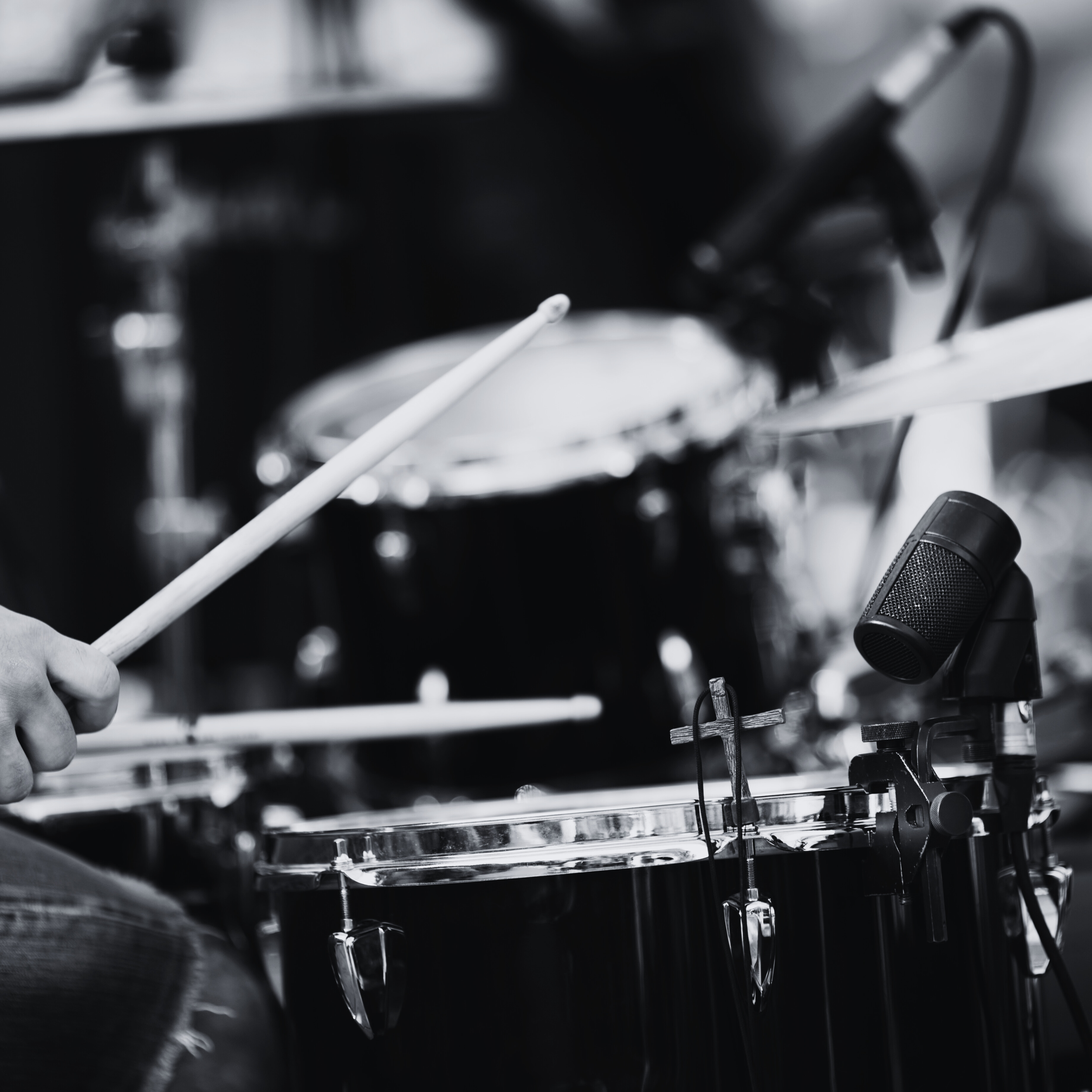A person playing a drum set, holding drumsticks over a snare drum with a microphone nearby in a music studio or stage setting.