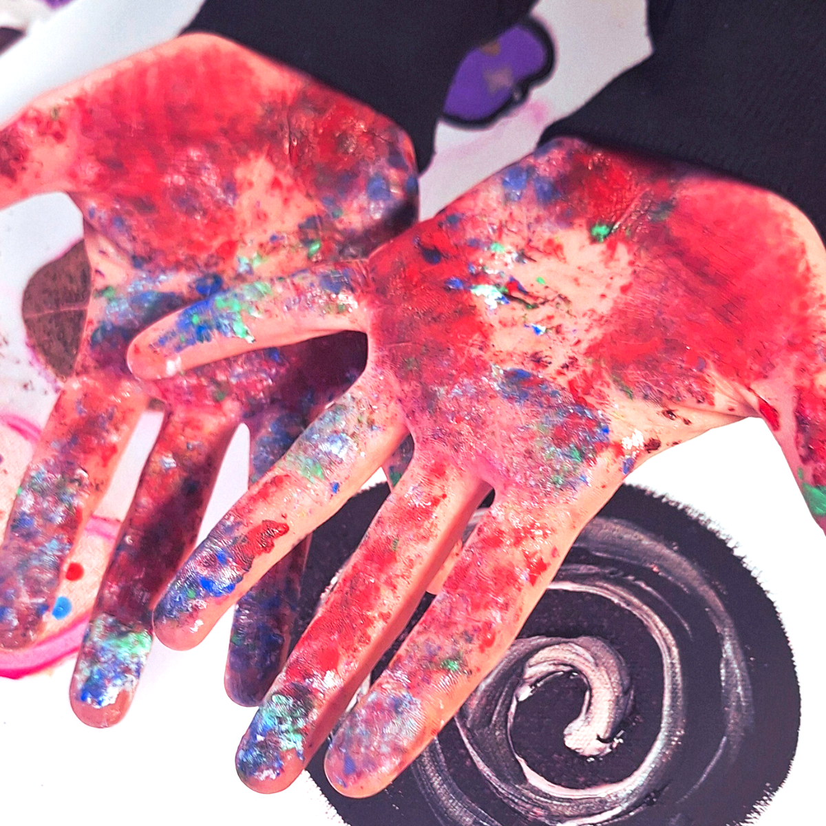 Paint-covered hands with colorful splatters and a skateboard wheel in the background.