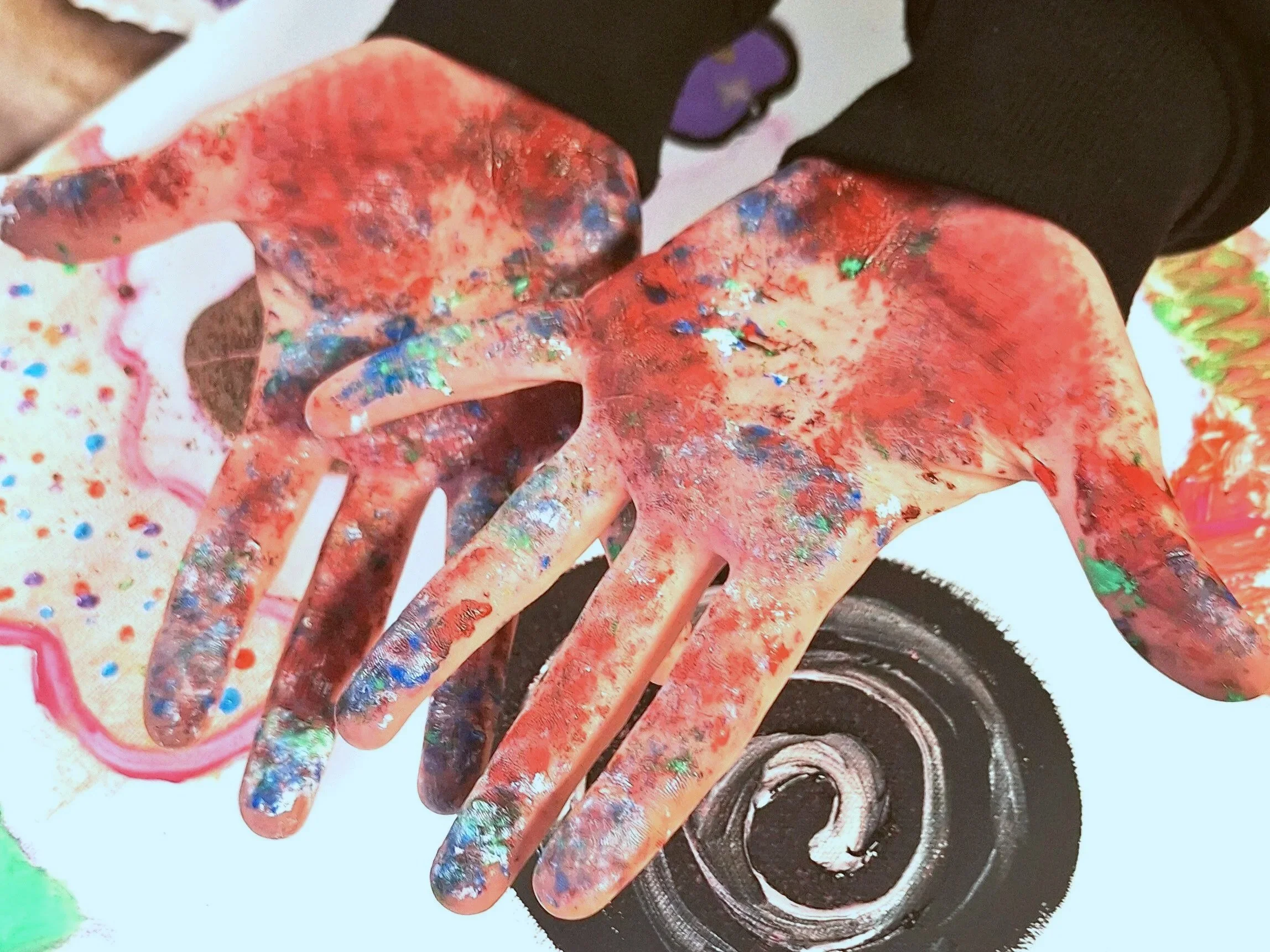 Close-up of a multicolored, splattered hand with a black gear-shaped object nearby.