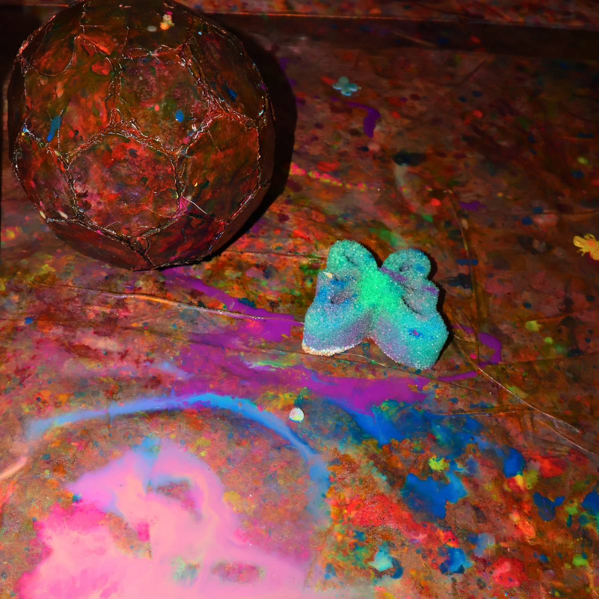 Colorful abstract art with a spherical object and a small, butterfly-shaped object on a multicolored, paint-splattered surface.