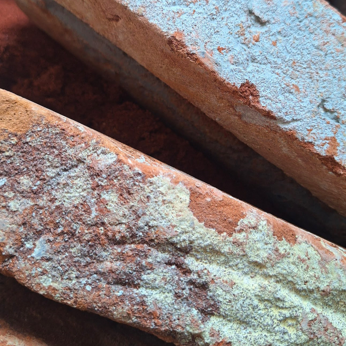 Close-up of weathered red bricks with chipped paint and surface buildup.
