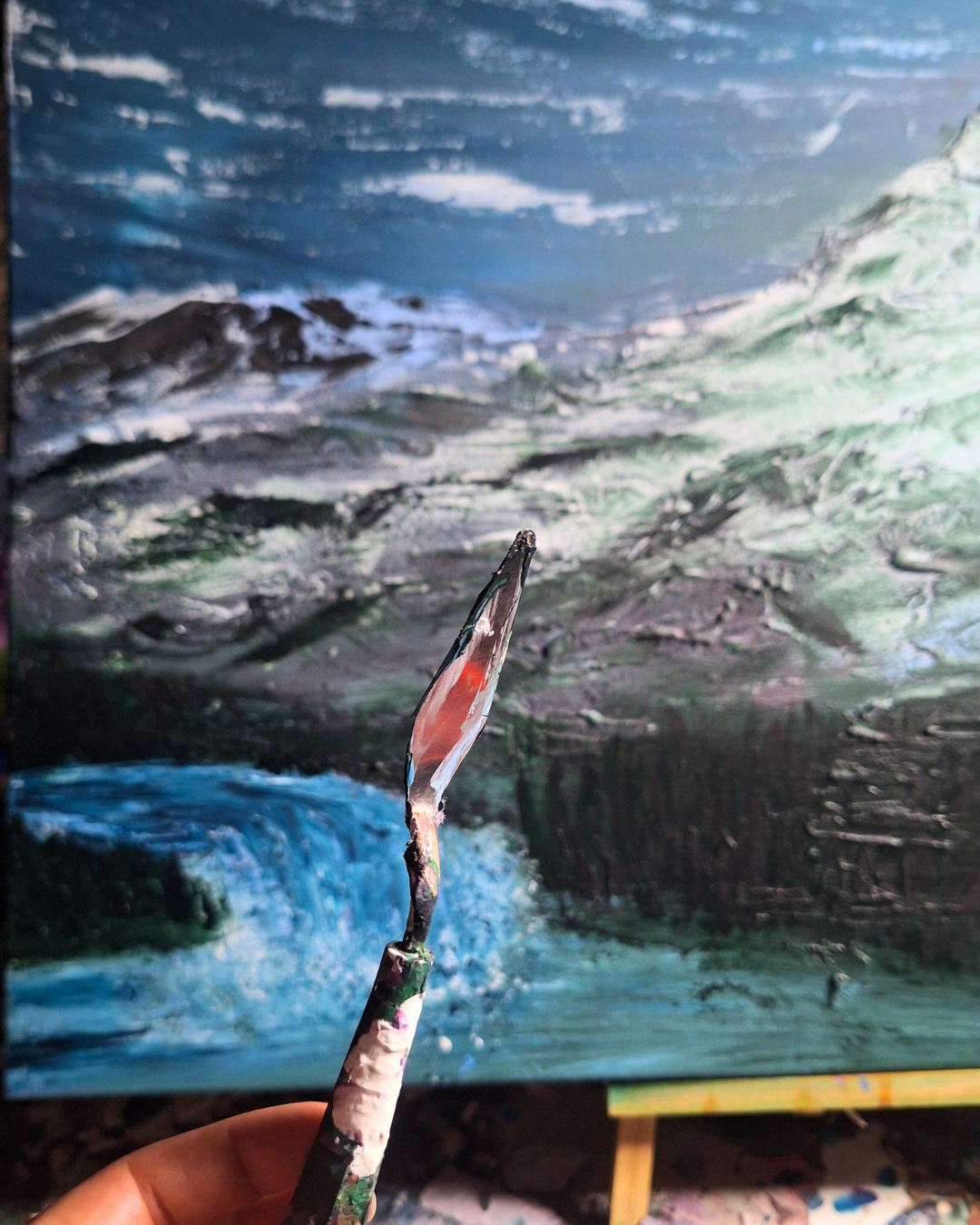 Artistic painting of a landscape with mountains, ocean waves, and sky, created with thick, textured brushstrokes.