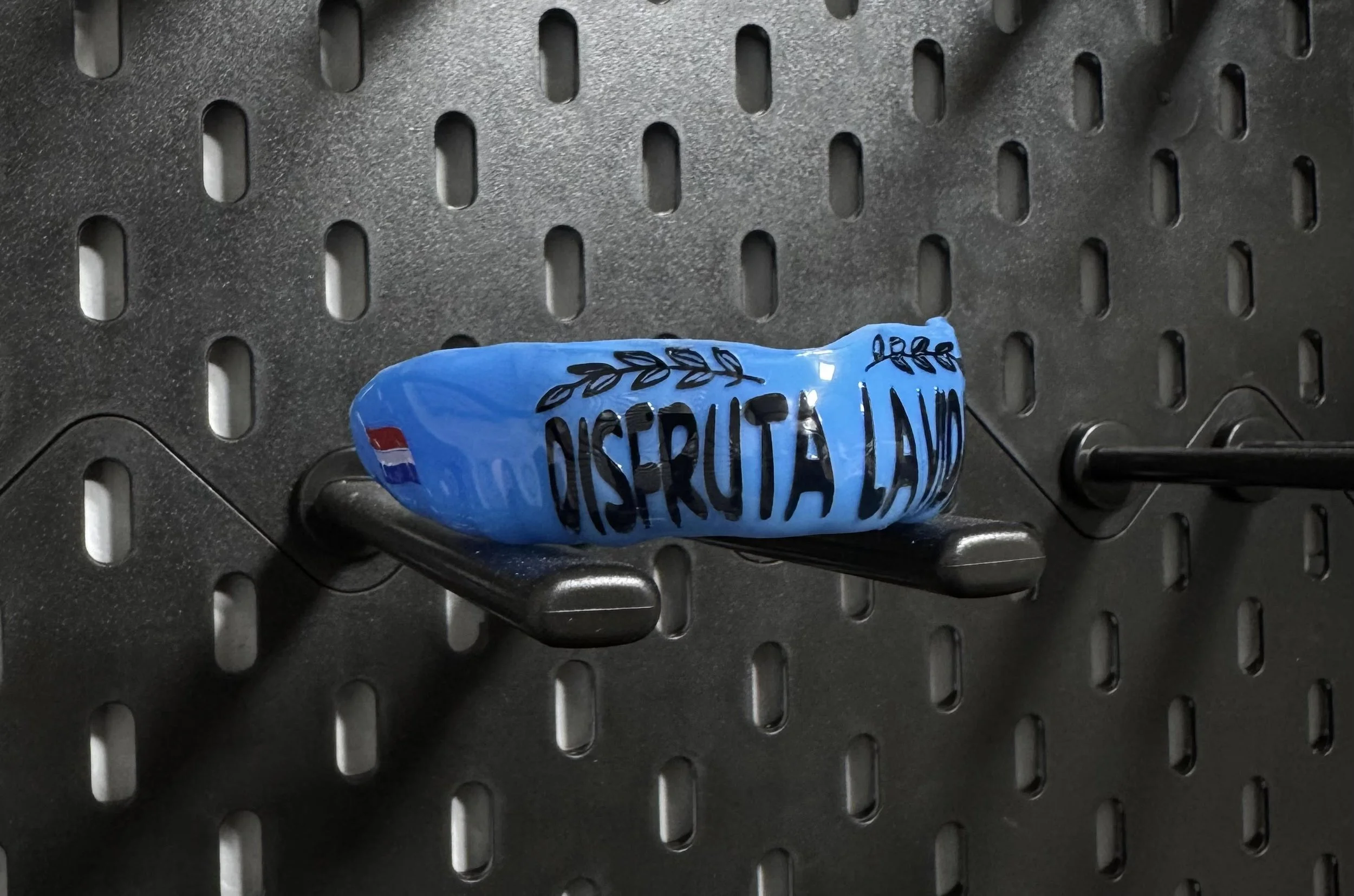 Blauwe snackverpakking met de tekst 'Disfruta La Vida' op een zwart geperforeerd oppervlak.