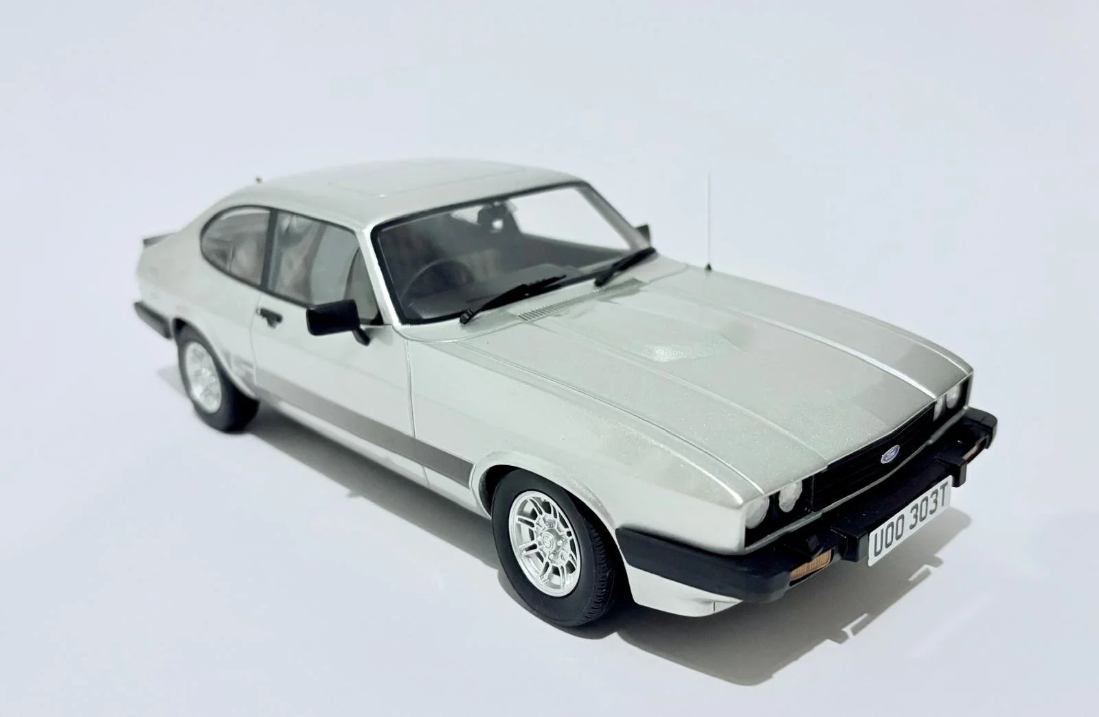 A scale model of a silver vintage Ford car on a white background.