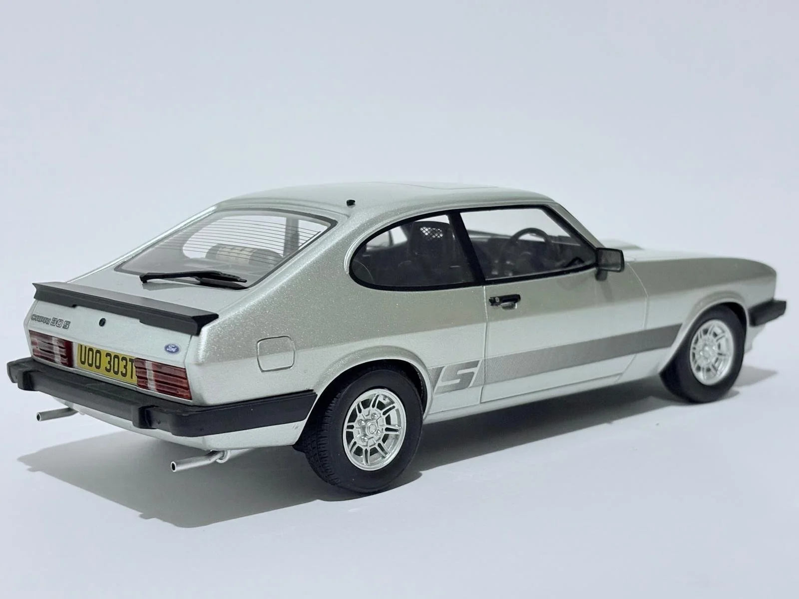 A detailed scale model of a classic Ford Escort 1.3 S car in silver with racing stripes and a rear spoiler, positioned on a plain white background.