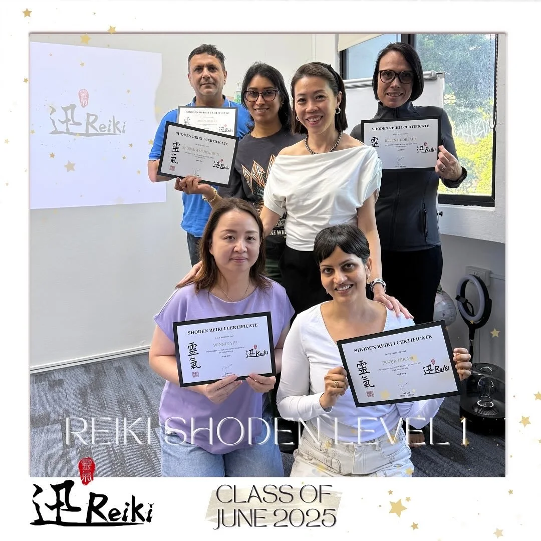 Group of six women and one man in a classroom, holding certificates from the Shoden Reiki Level 1 course, with a whiteboard and window in the background, celebrating their graduation in June 2025.