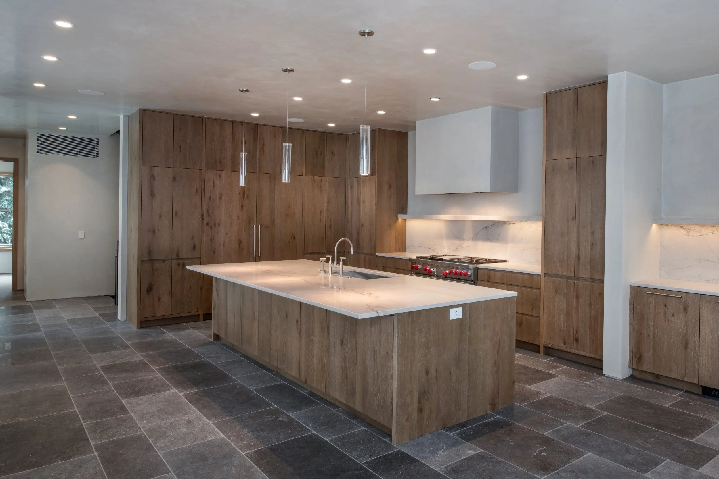 Modern kitchen with wood cabinets, a large island with a white marble countertop, pendant lights, and a stainless steel stove.