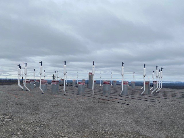 Grey piles that will form part of the foundation of the wind turbine have been installed at the site. Thermosyphons (white poles) will help to protect the thermafrost beneath and around the turbine as well as help stabilize the structure.