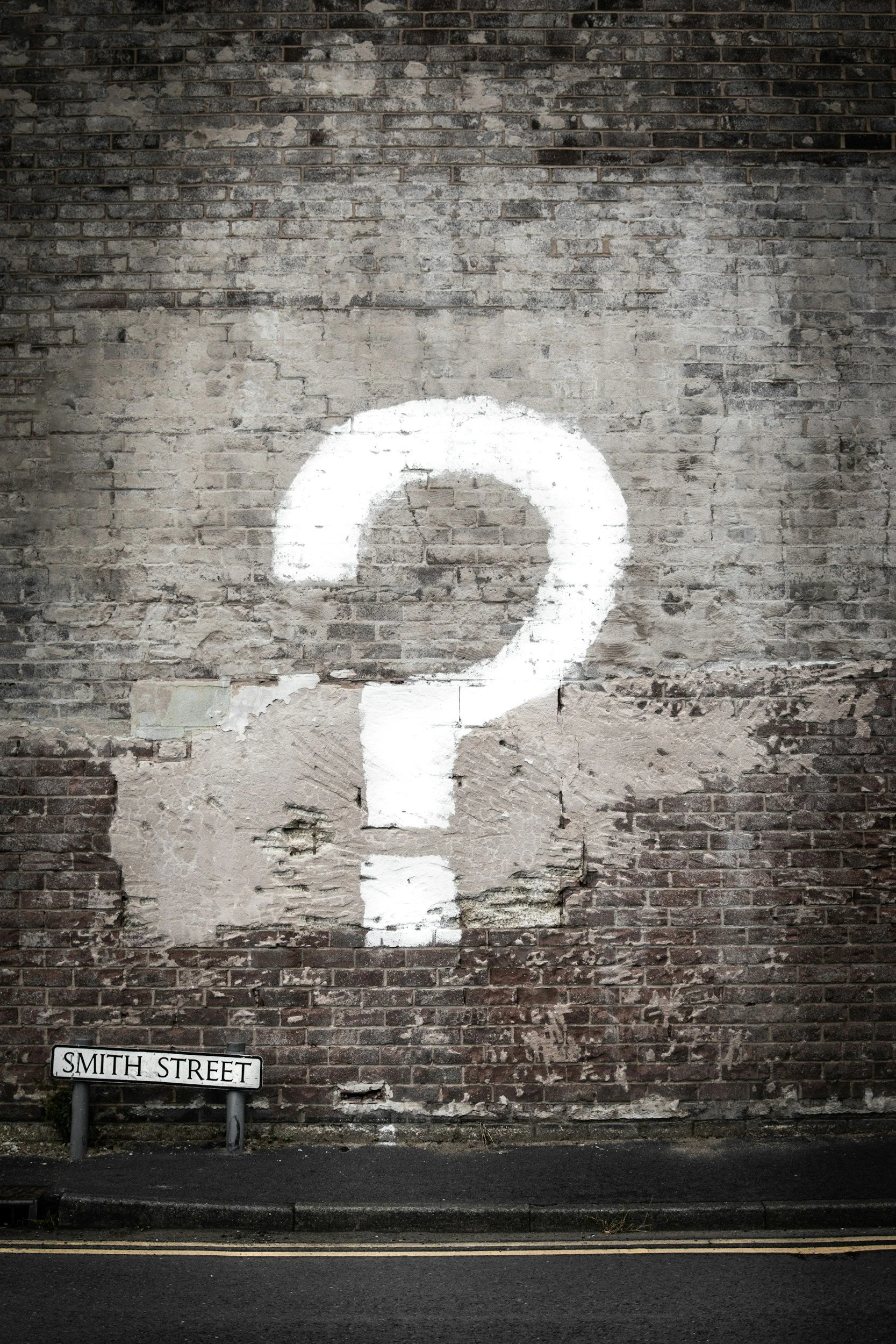 A large white question mark painted on a weathered brick wall with a street sign that reads Smith Street.