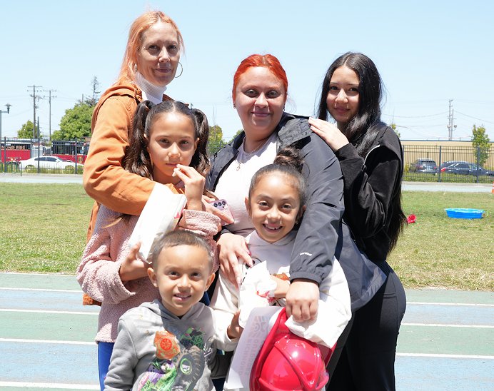 Group of six females, including children, standing outdoors on a sports field, smiling and posing for the photo.