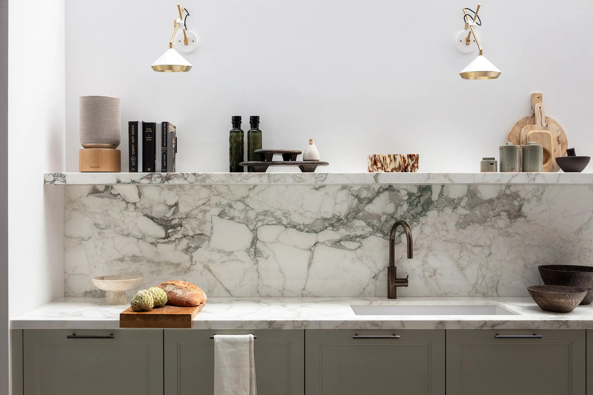 Detailed kitchen vignette featuring honed marble splashback, integrated basin, and curated shelf styling with warm brass accents, designed by the studio.