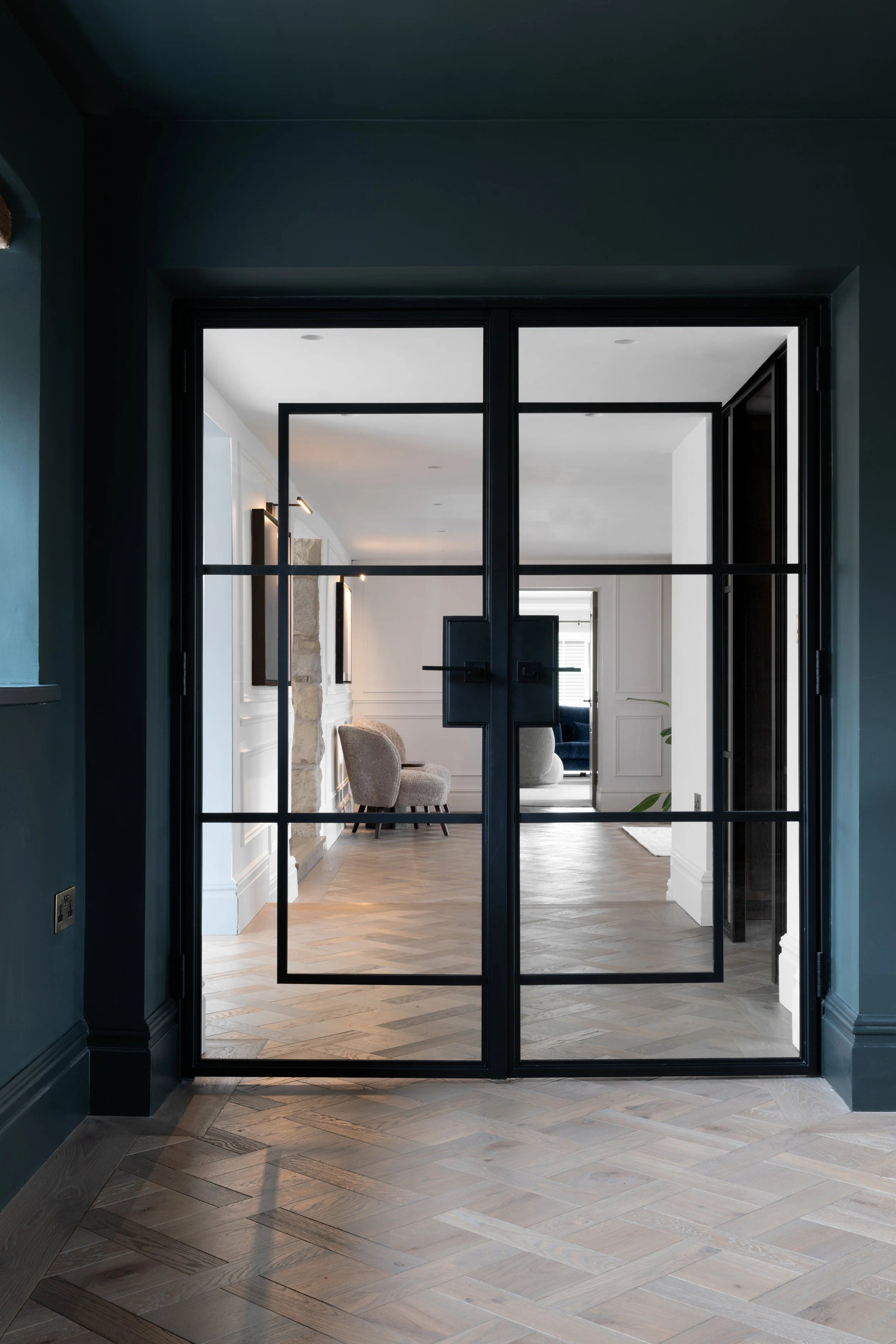 Black-framed steel and glass double doors opening into a herringbone-floored hallway