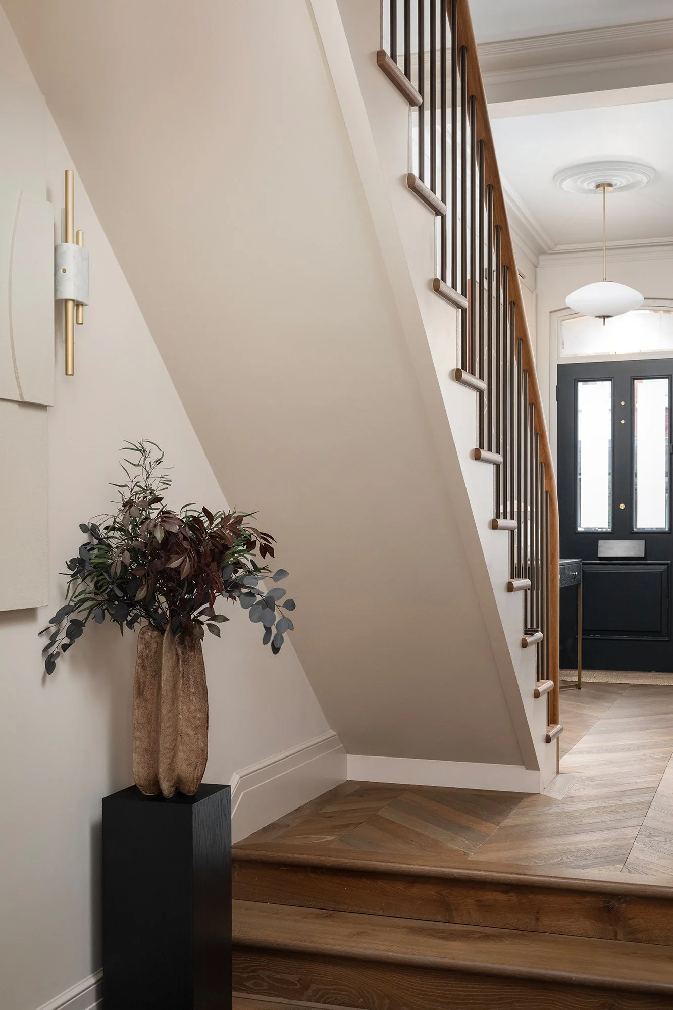 Refined hallway with sculptural staircase detailing, soft neutral walls, and a textured vessel arrangement designed by the studio.