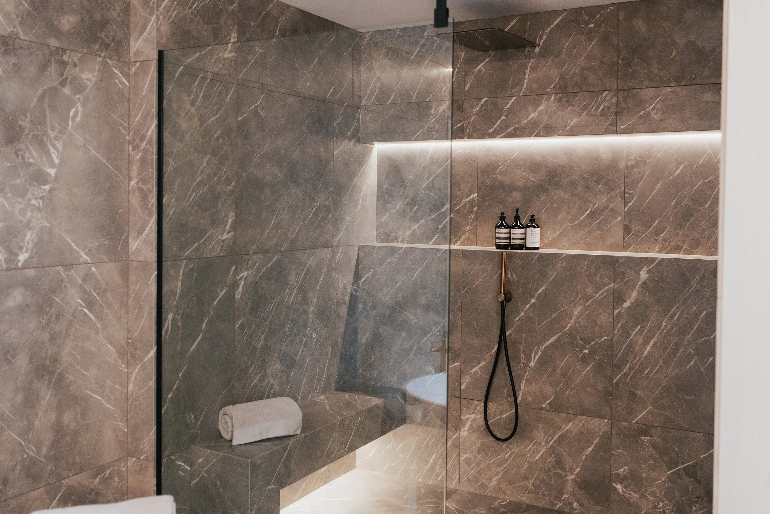 Walk-in shower with marble-effect tiles, built-in bench seating, glass screen and concealed LED lighting