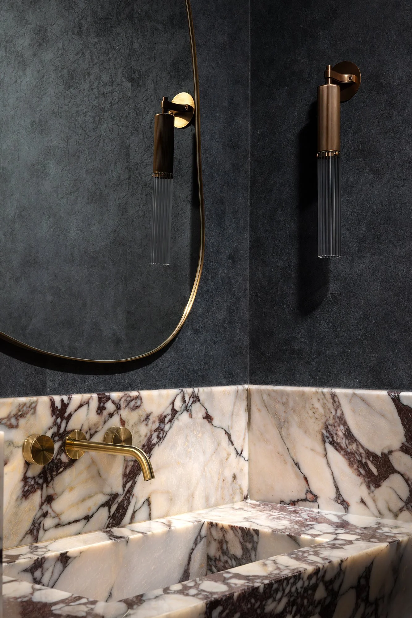 Atmospheric powder room with dark textured walls, sculptural brass fittings, and expressive marble basin detailing designed by the studio.