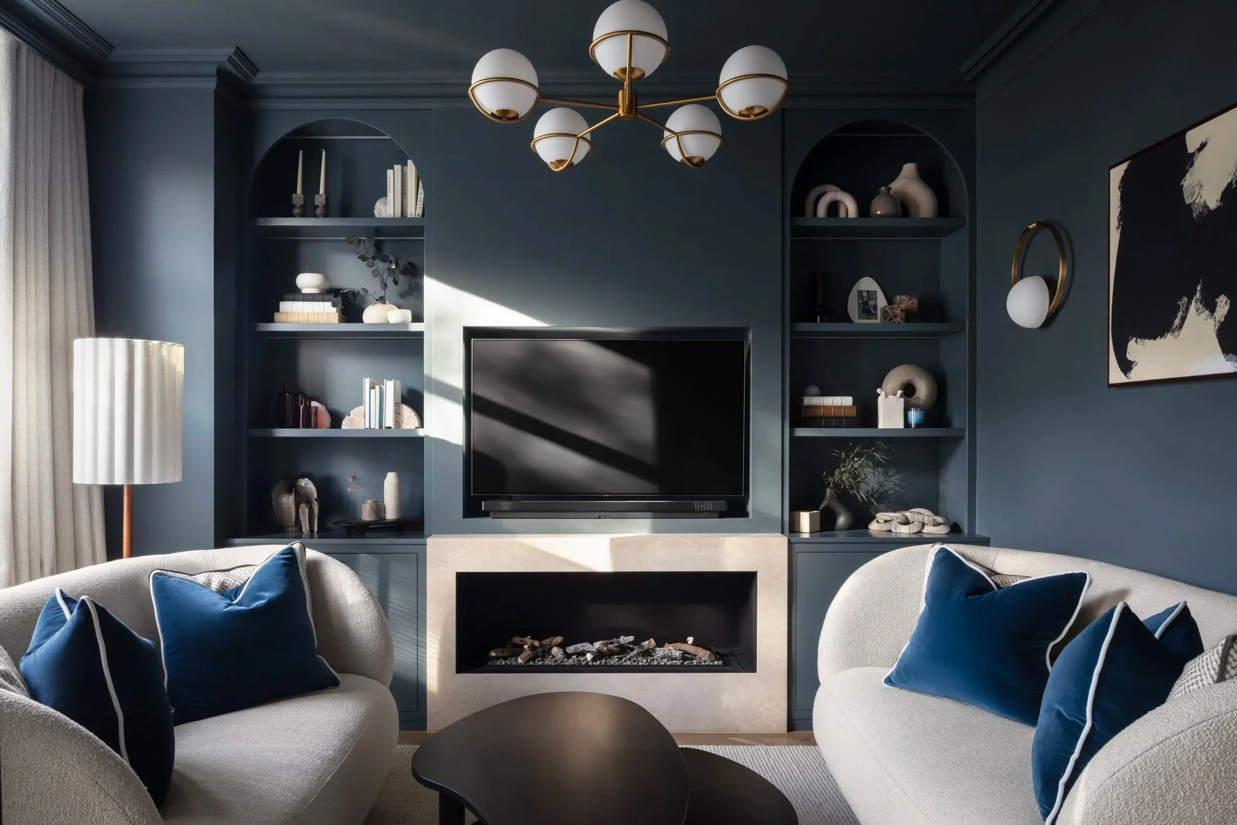 Bespoke living room design featuring deep blue cabinetry, curated shelving, contemporary fireplace detailing, and soft curved seating by the studio.