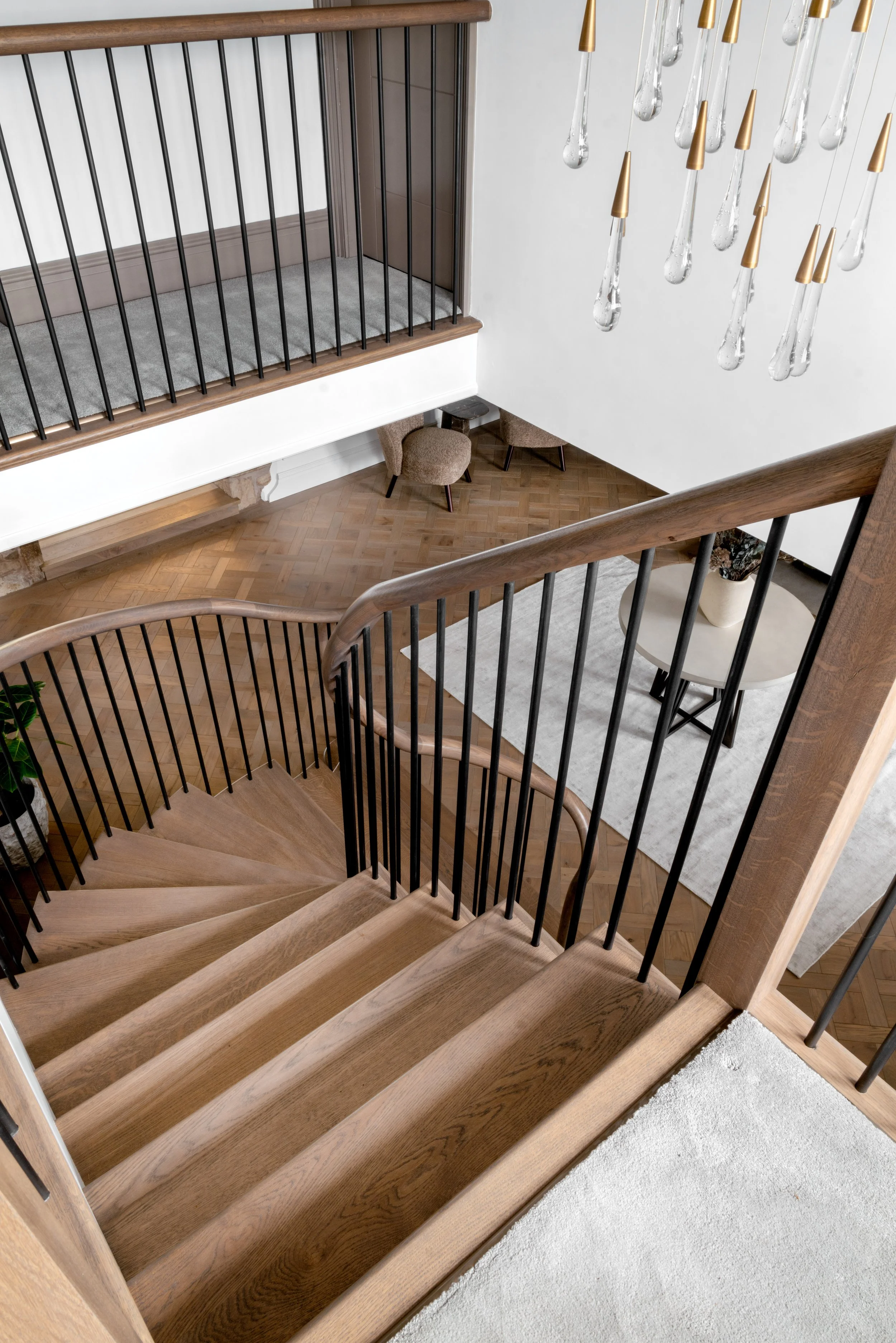 Curved oak staircase with black metal balustrade overlooking herringbone timber flooring and double-height hallway