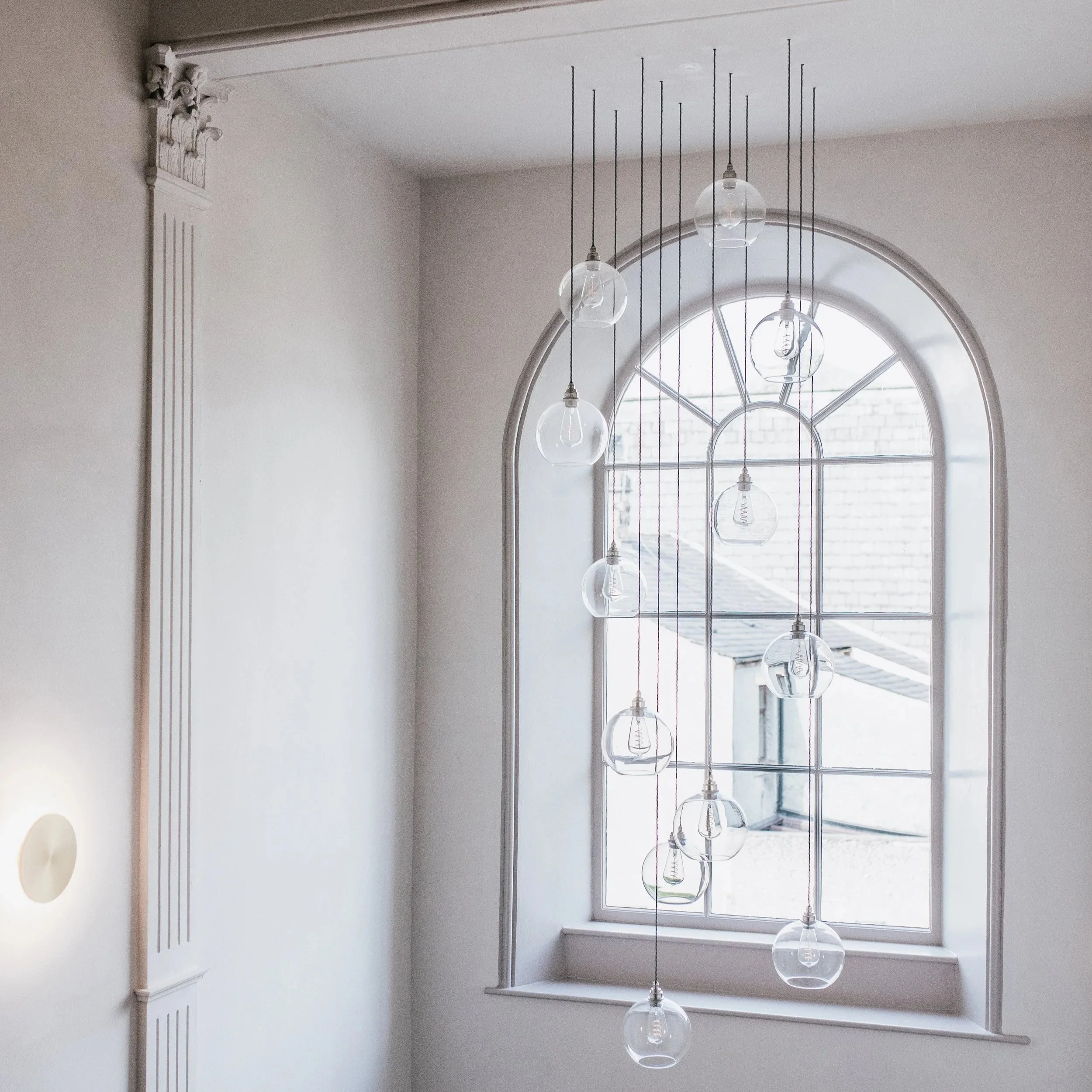 Arched window with cascading glass pendant lights in double-height stairwell