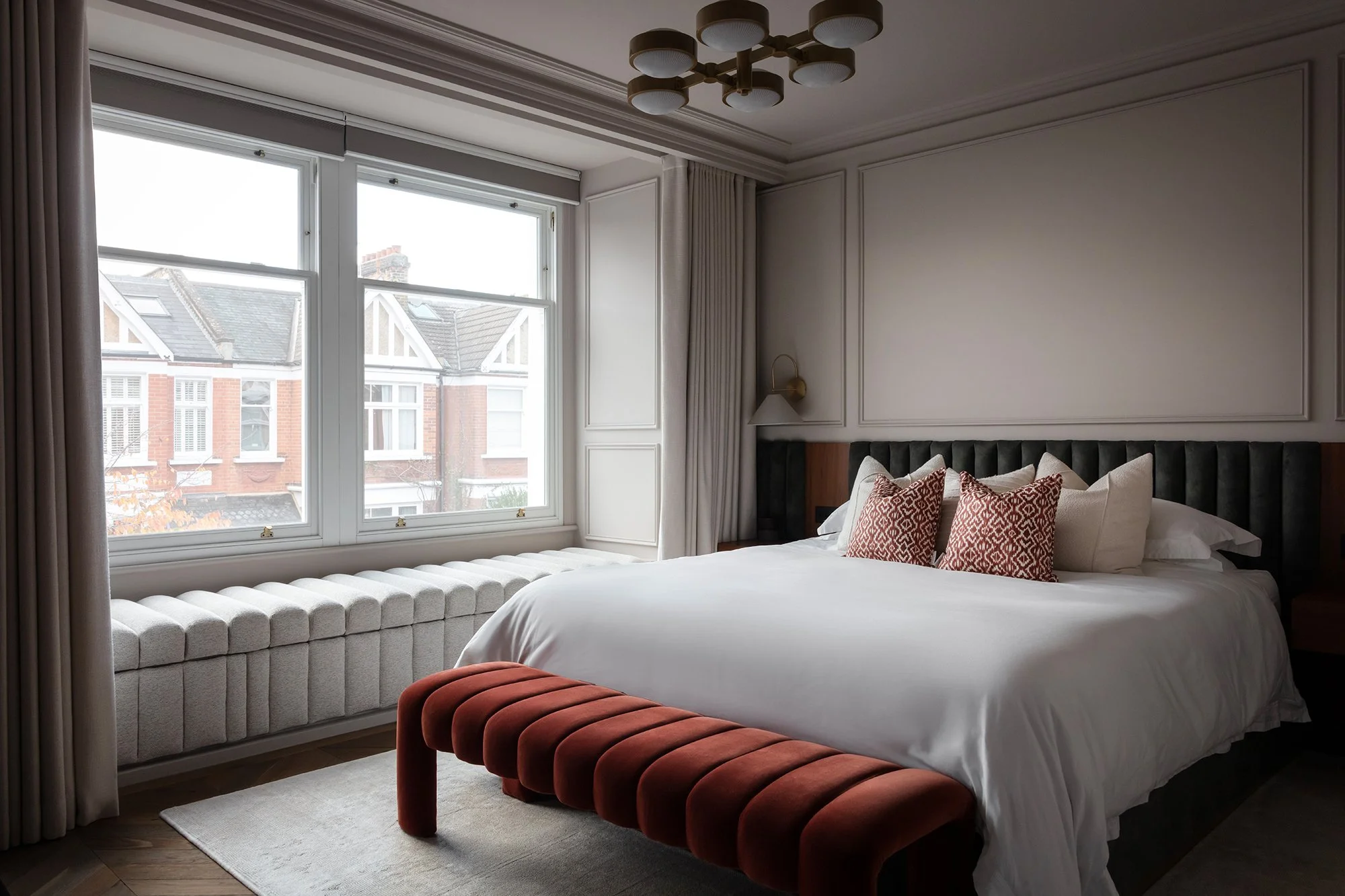 Elegant bedroom with tailored wall panelling, a velvet channelled bench, soft layered bedding, and refined detailing designed by the studio.