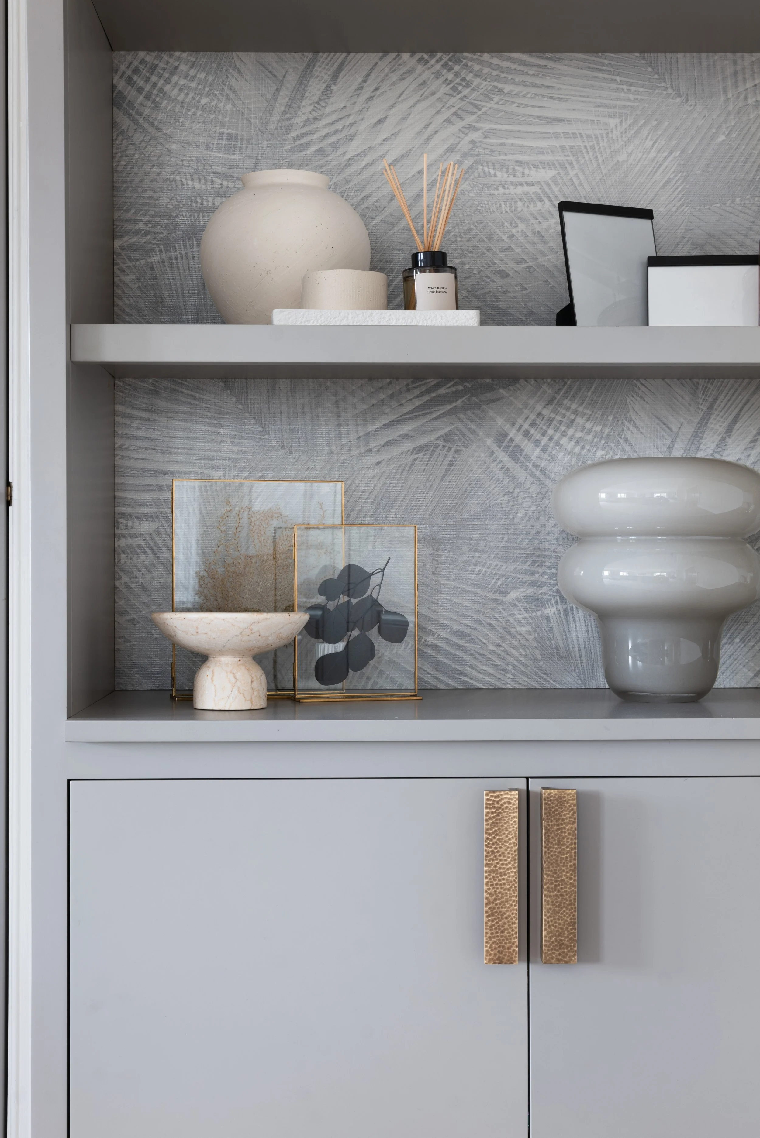 Detail of bespoke shelving with textured wallpaper backing, sculptural objects and brass cabinet handles
