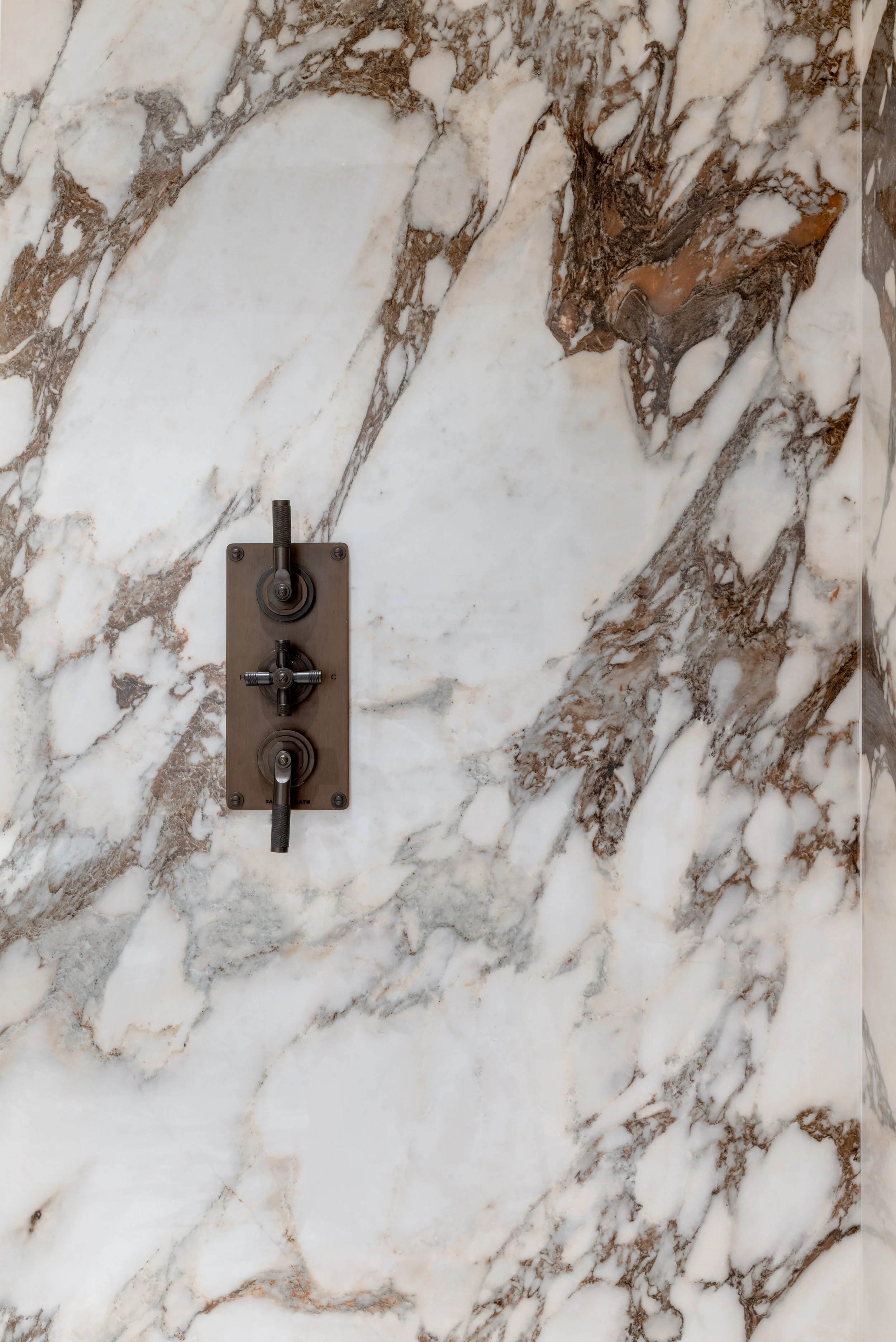 Concealed shower controls set into veined marble wall with aged bronze fittings
