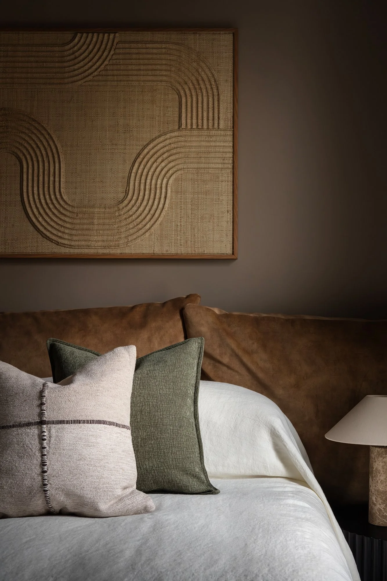 Textural bedroom detail featuring layered neutral linens, earthy cushions, and bespoke woven wall art designed by the studio.