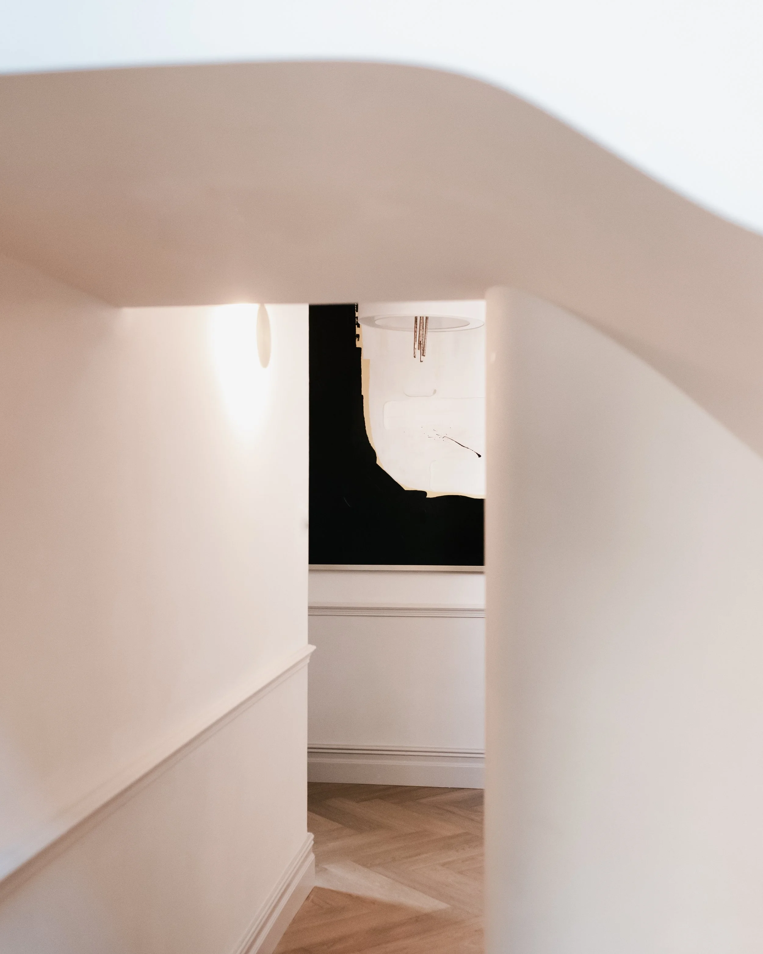 Curved hallway with arched ceiling, wall lighting and framed artwork above herringbone timber flooring