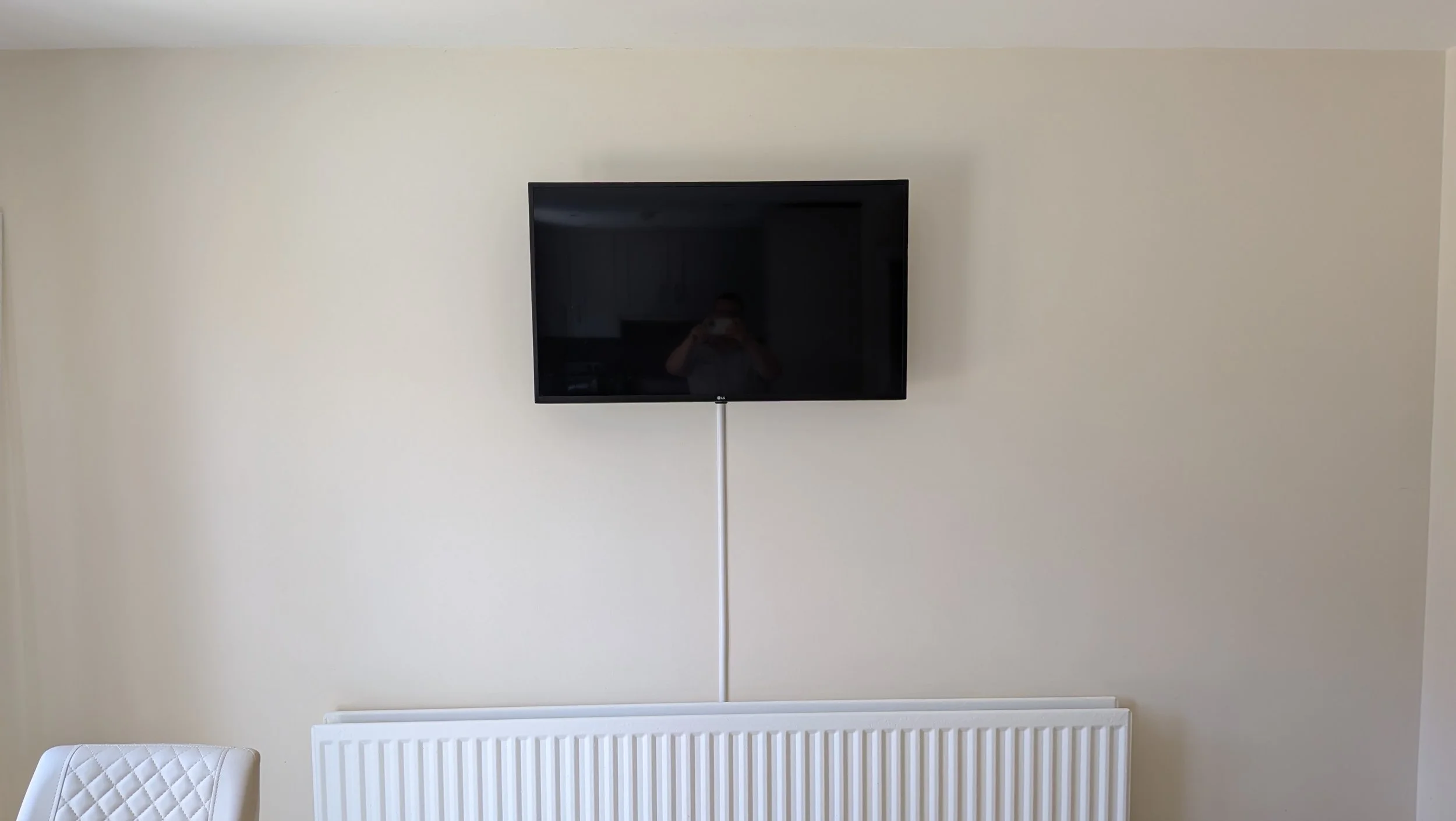 TV & Audio: Flat screen TV mounted on a beige wall above a white radiator, wires trunked from TV to socket - Ballygowen