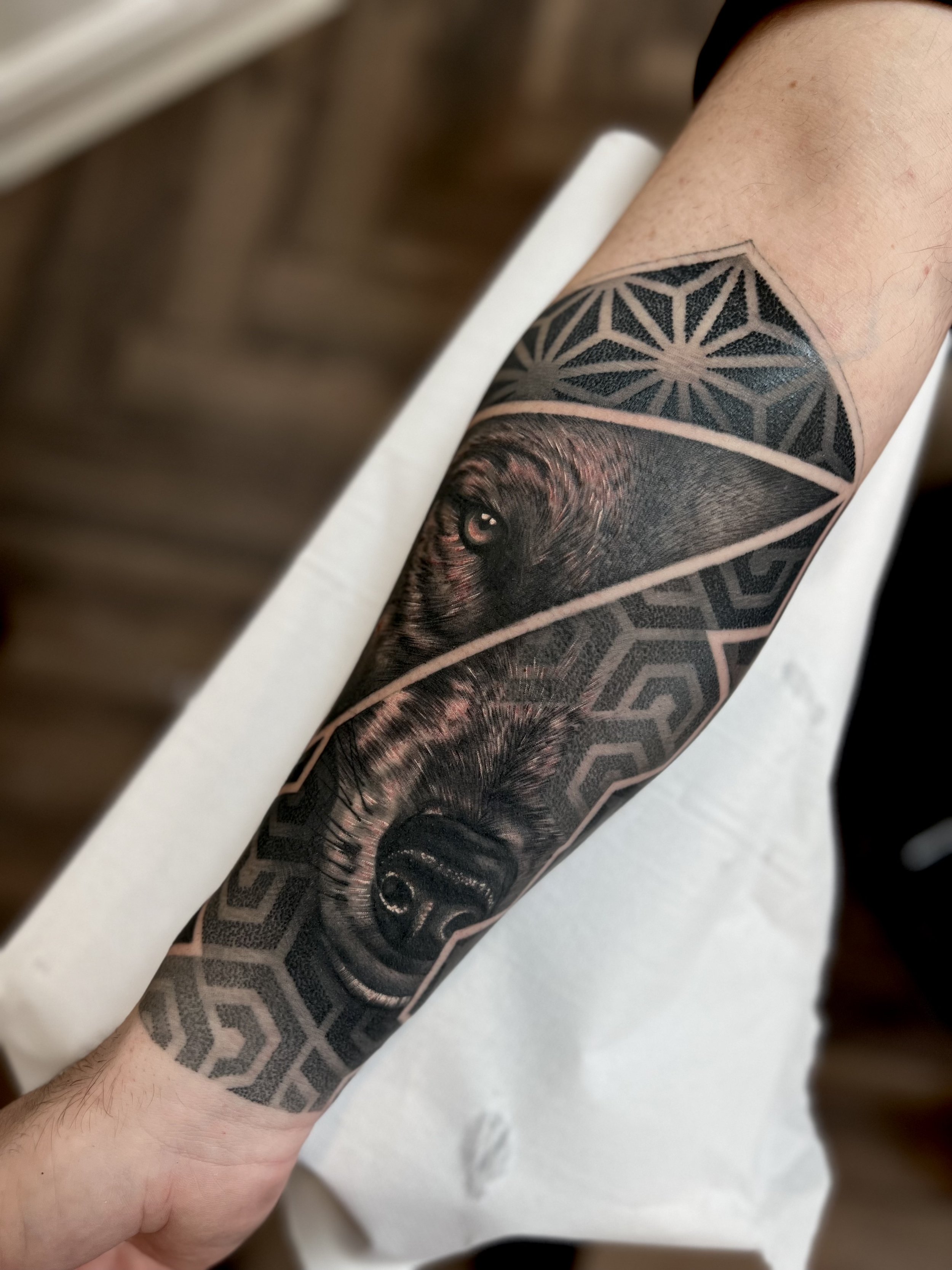 Black and grey tattoo of a wolf's face on a person's arm, with geometric patterns above and below the wolf's head.