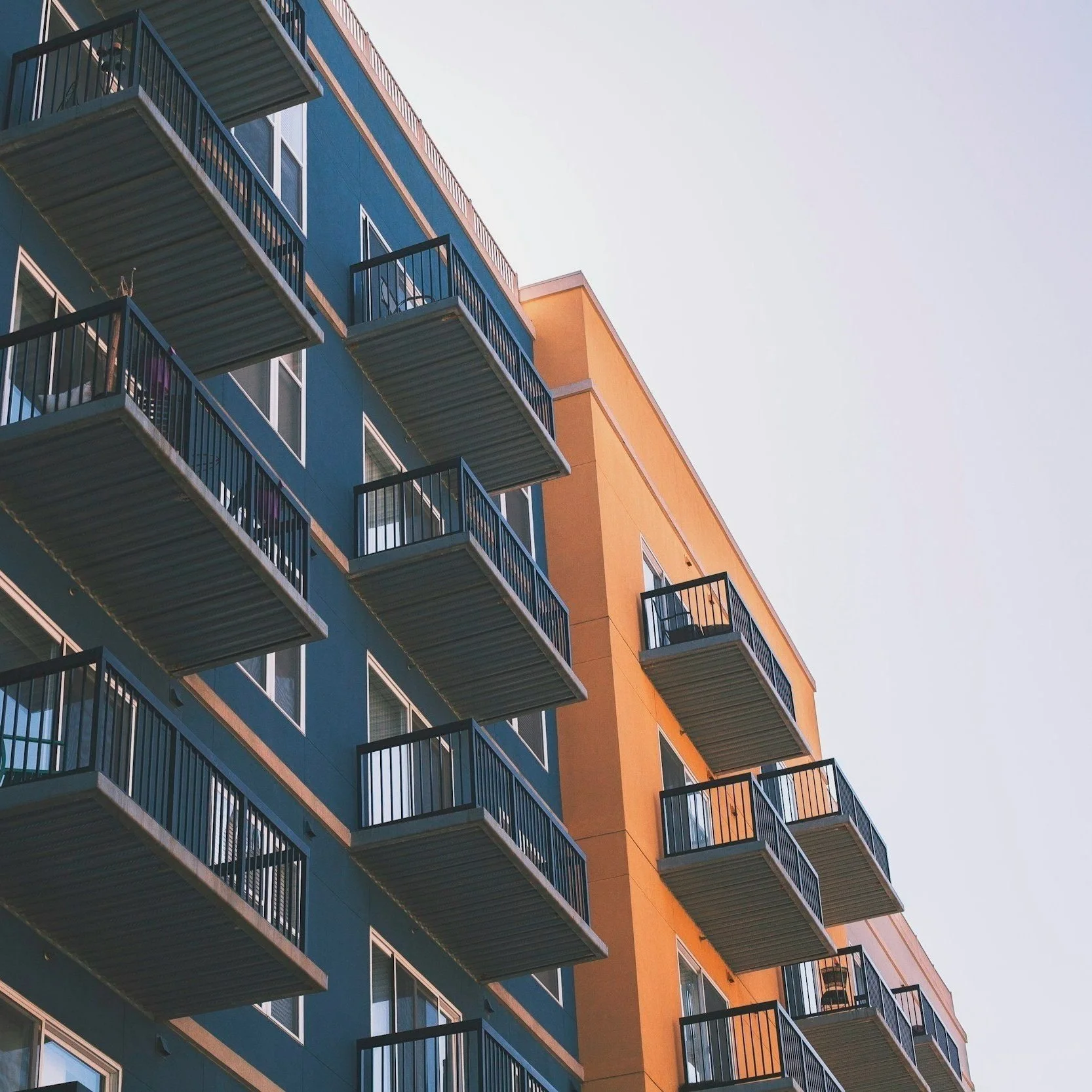 Multiple apartment balconies with black railings on a blue and orange building under a clear sky.