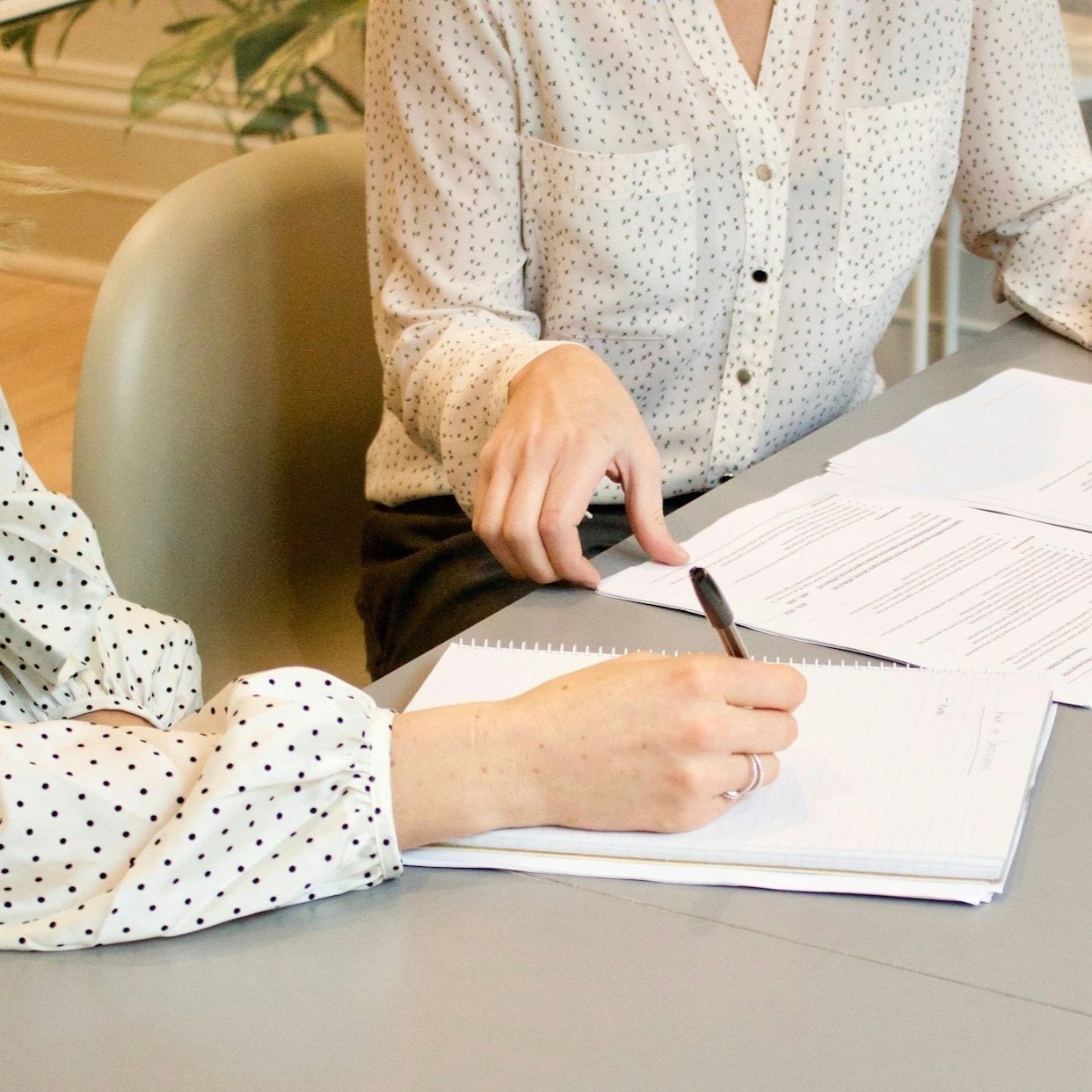 Two people in polka dot shirts are working with documents and a notepad on a grey table.