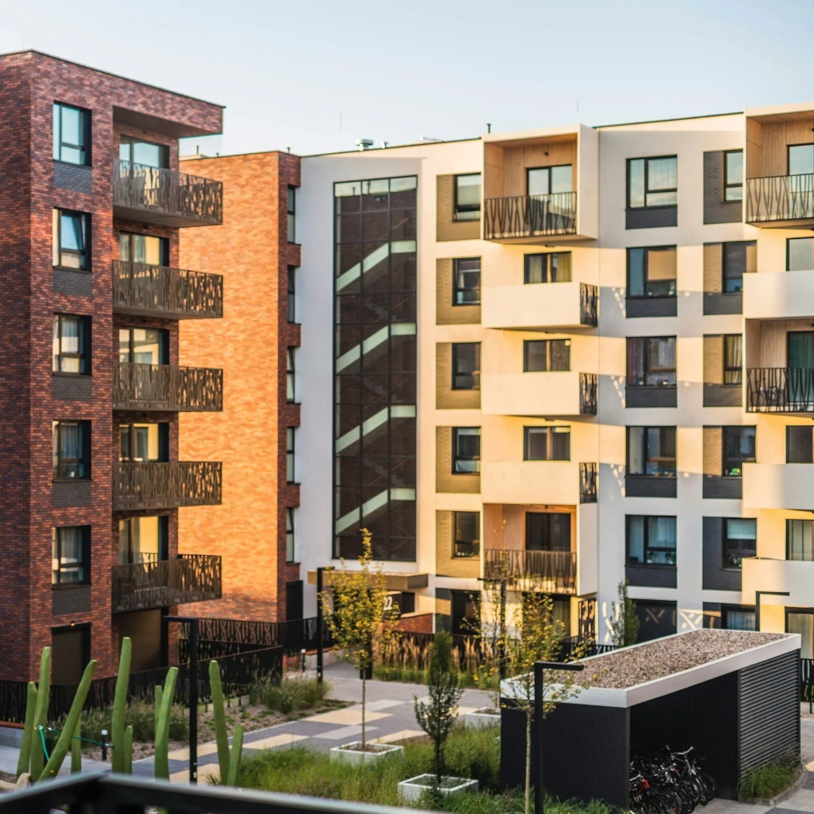 Modern multi-story apartment buildings with balconies, a landscaped courtyard, and a bike storage shed.