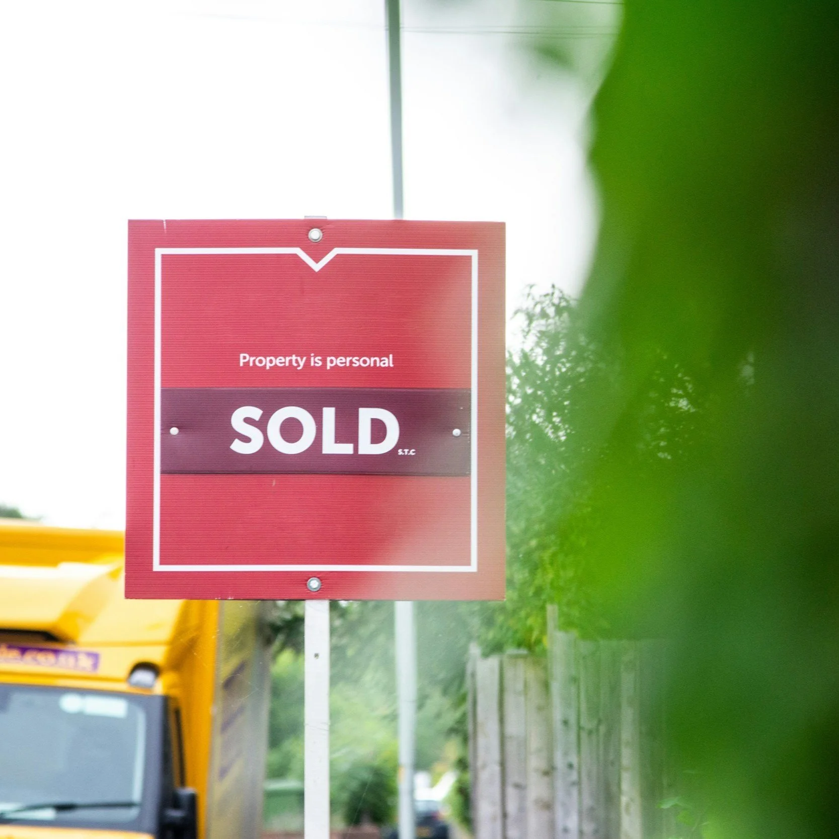 A red and white sign that reads "Property is personal, SOLD." The sign is on a pole beside a street, with a yellow vehicle partially visible in the background and some greenery in the foreground.