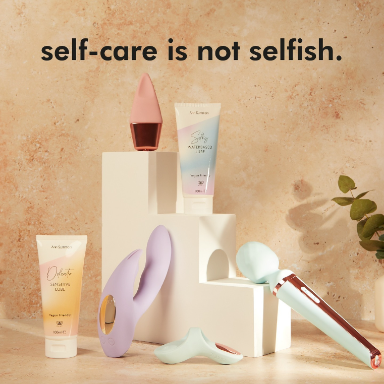 An assortment of self-care and personal wellness devices and products displayed on white pedestals, with a background featuring the phrase 'self-care is not selfish.' in bold black text.