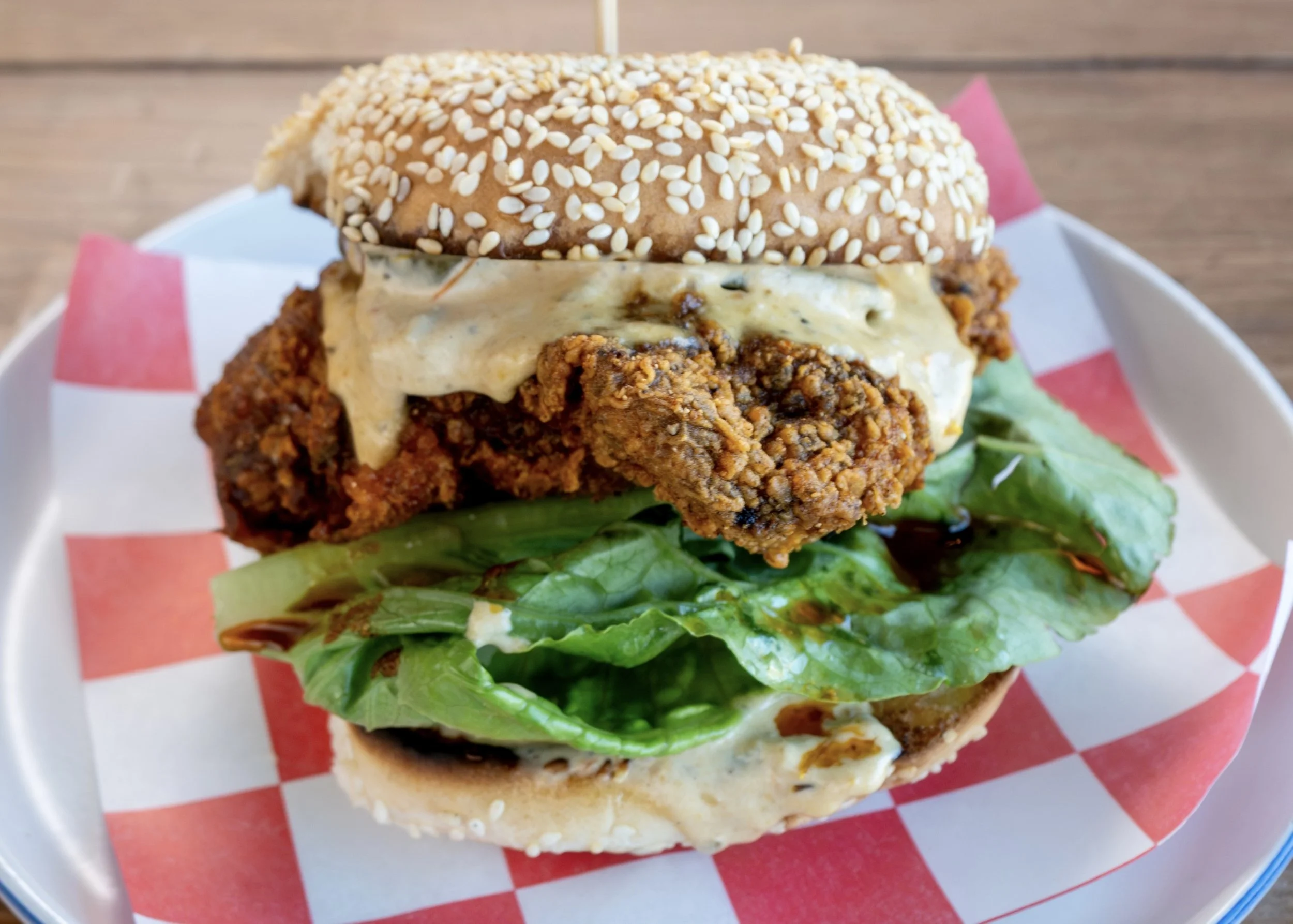 vegan nashville chicken made with house made vegan proteins and seeded bun served on checkered service paper on white plate