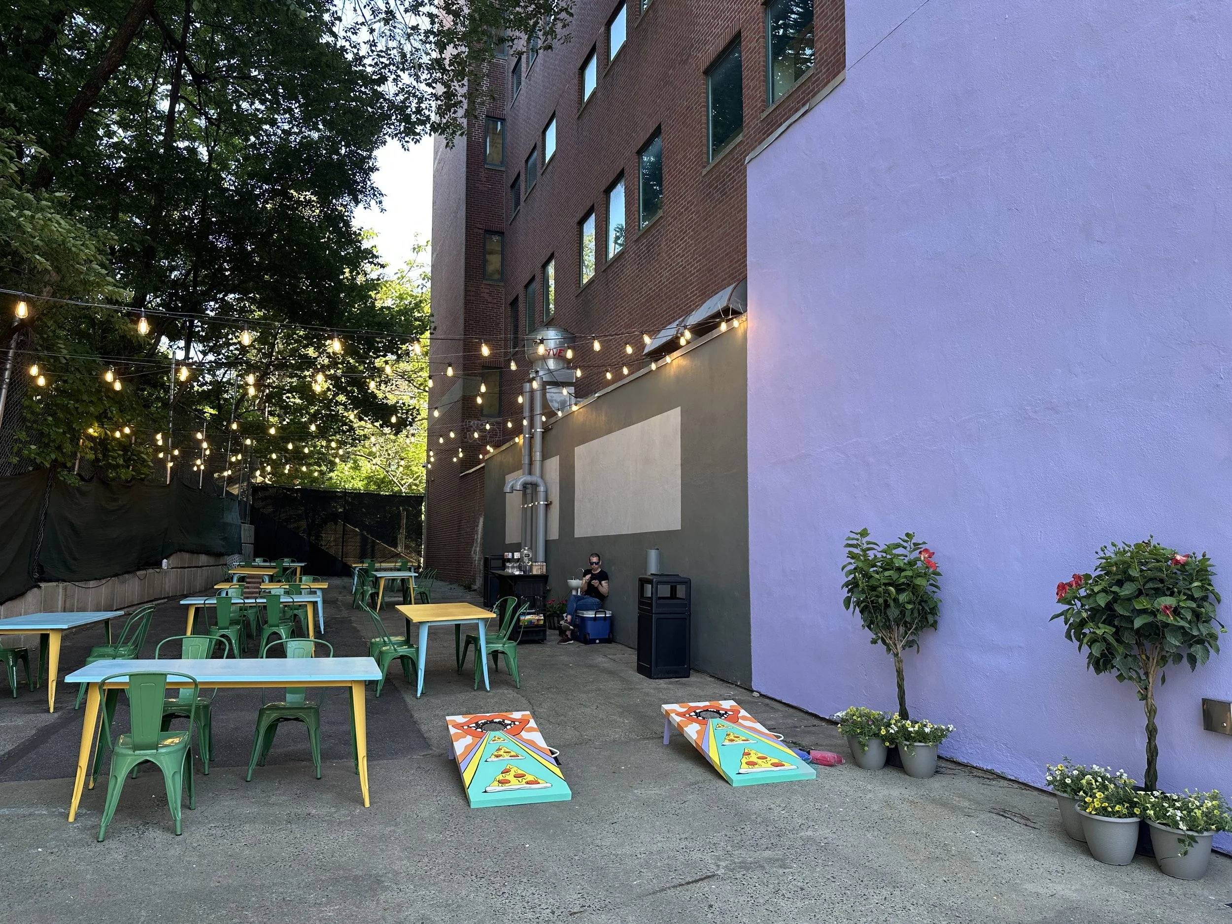 outdoor colorful, tree shaded patio at cerveau with tables, seats 50-70 people, bar and cornhole games 