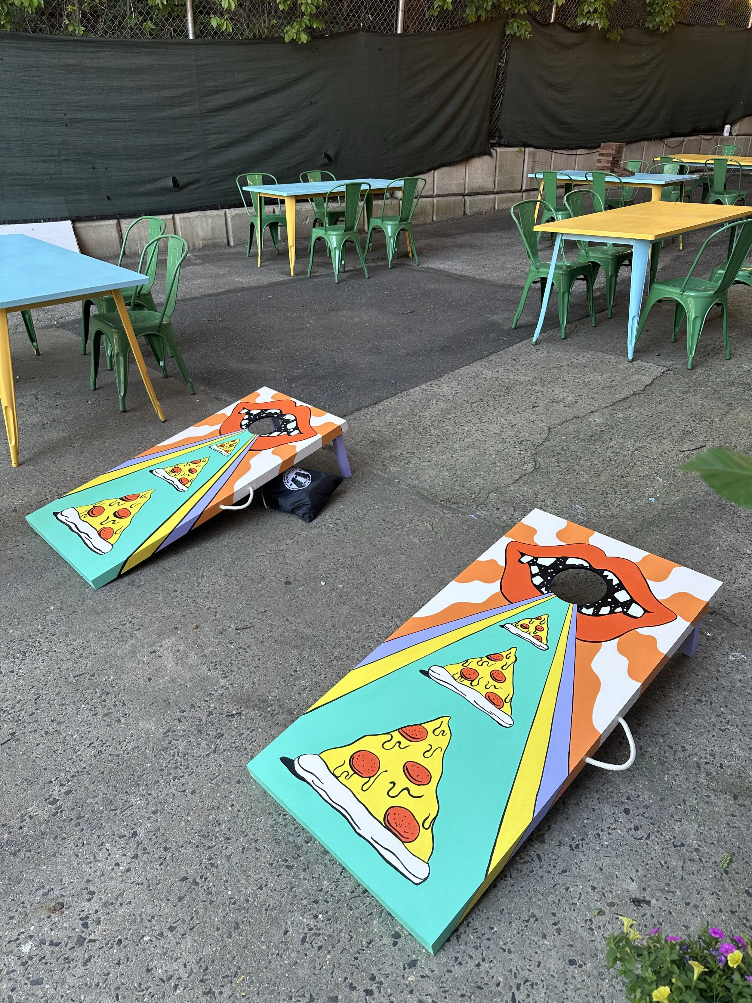outdoor tree shaded patio at cerveau with colorful tables, seats for 50-70 people, and cornhole games 