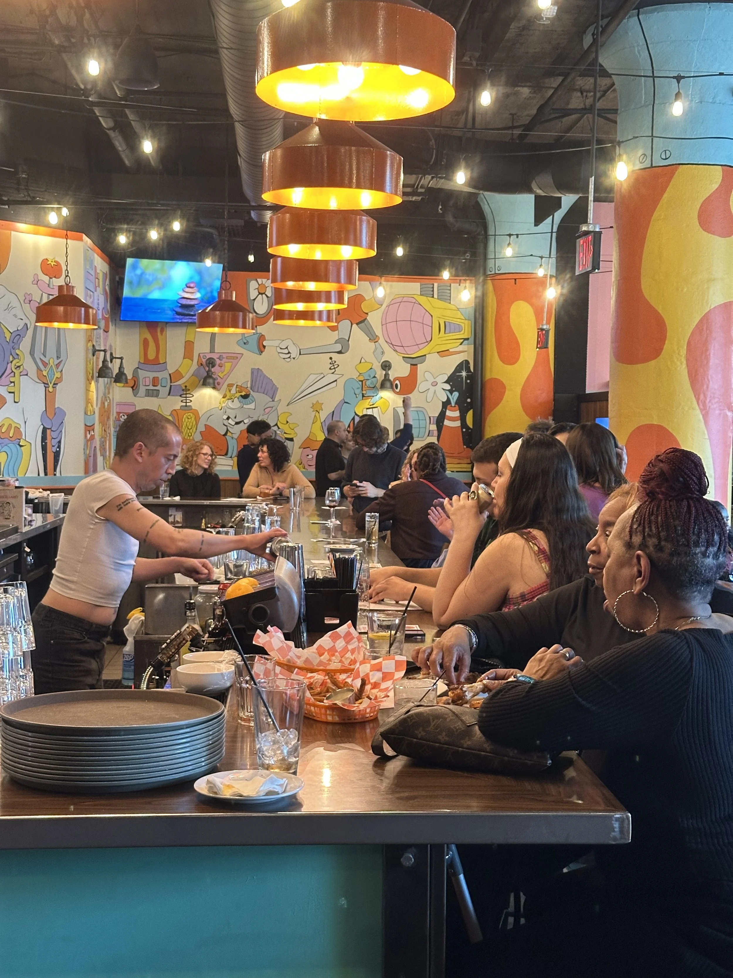 large group being served alcoholic and non-alcoholic beverages at bar inside brightly colored space before union transfer show
