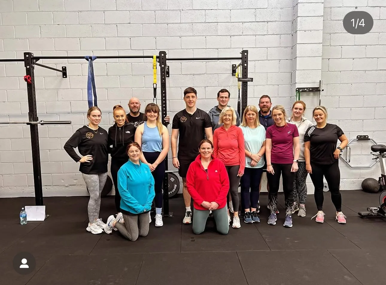 Group of diverse people in athletic wear posing together in a gym with workout equipment in the background.