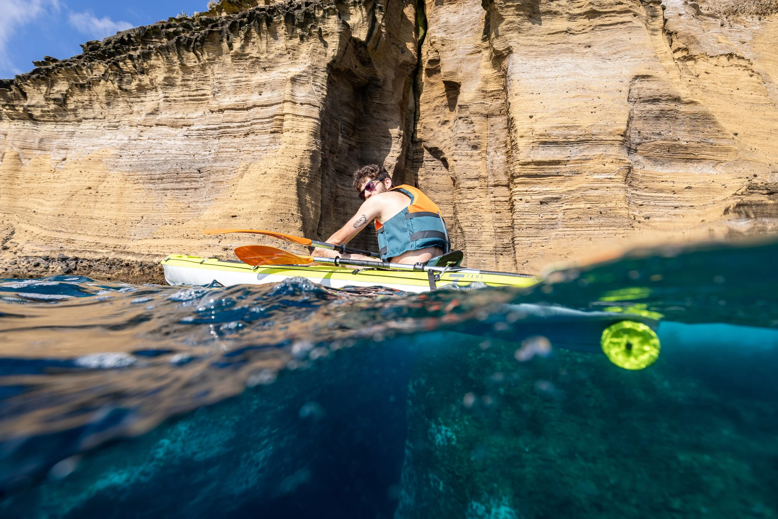 A person kayaking in the water near a steep, rocky cliff.