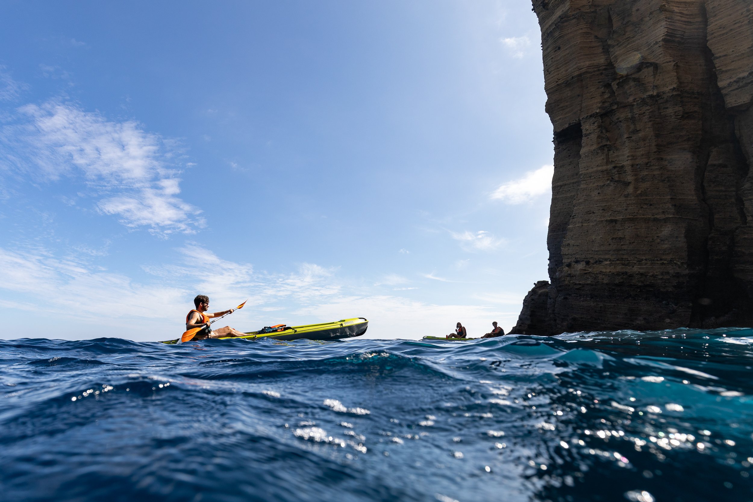 People kayaking near a rocky cliff on a sunny day.