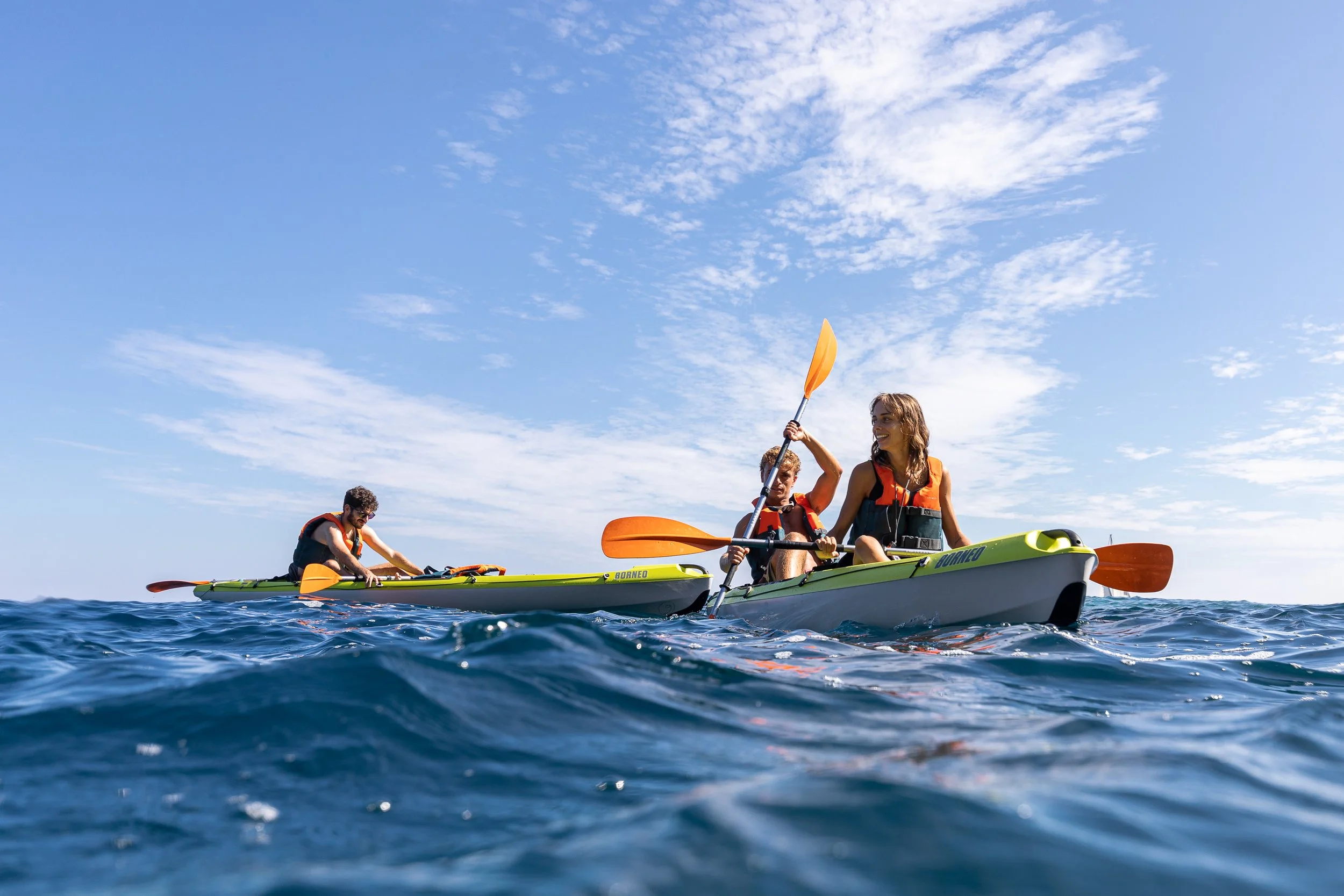 A group of people kayaking on the water under a clear blue sky with a few clouds, engaging in water sport activity on a sunny day.