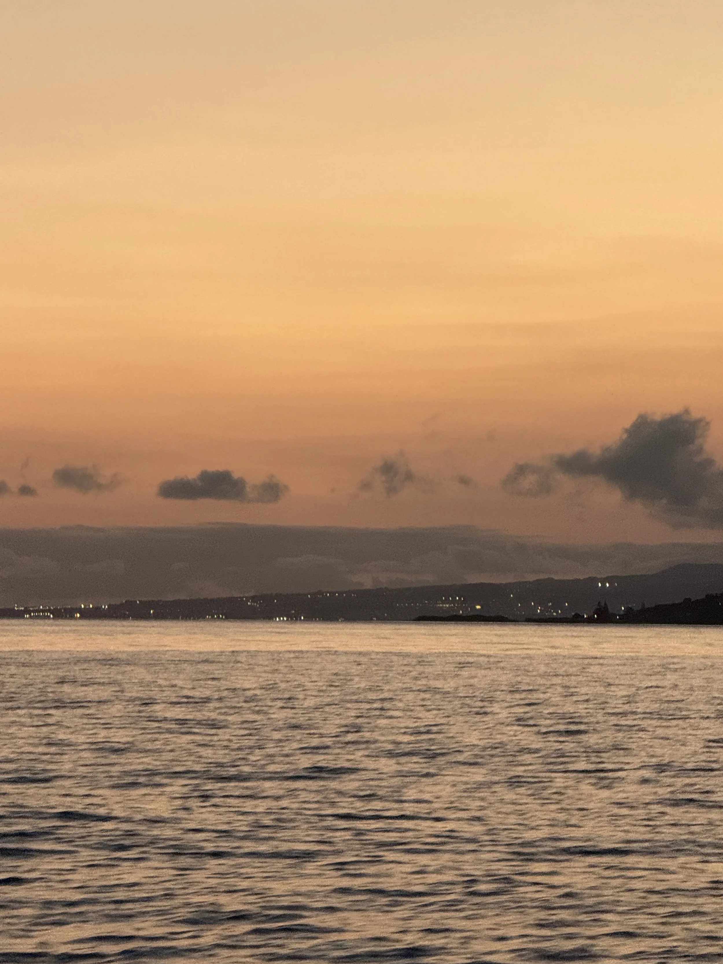 A sunset over a body of water with distant clouds and a silhouette of land.