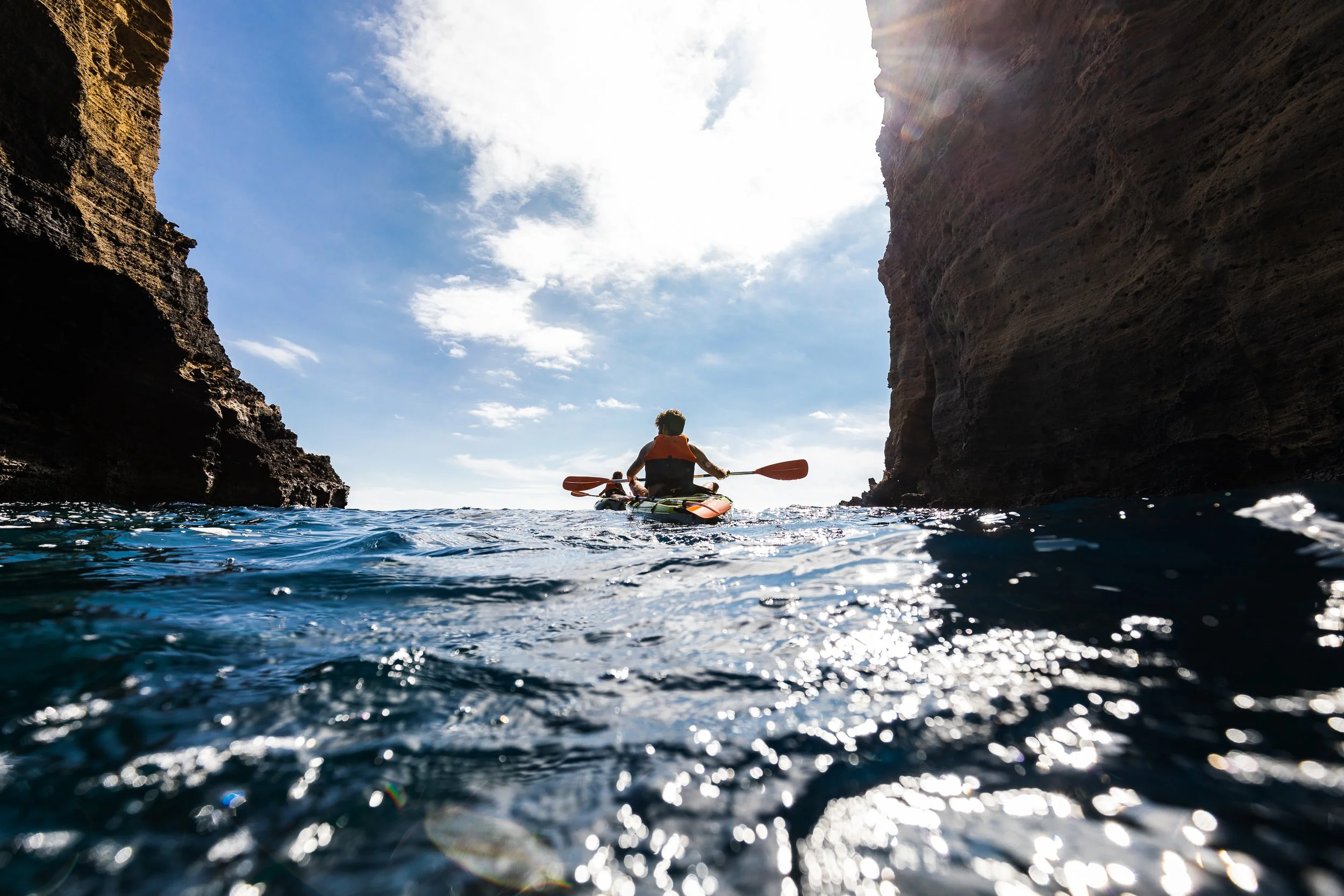 Person kayaking between large rock cliffs under partly cloudy sky during daytime.