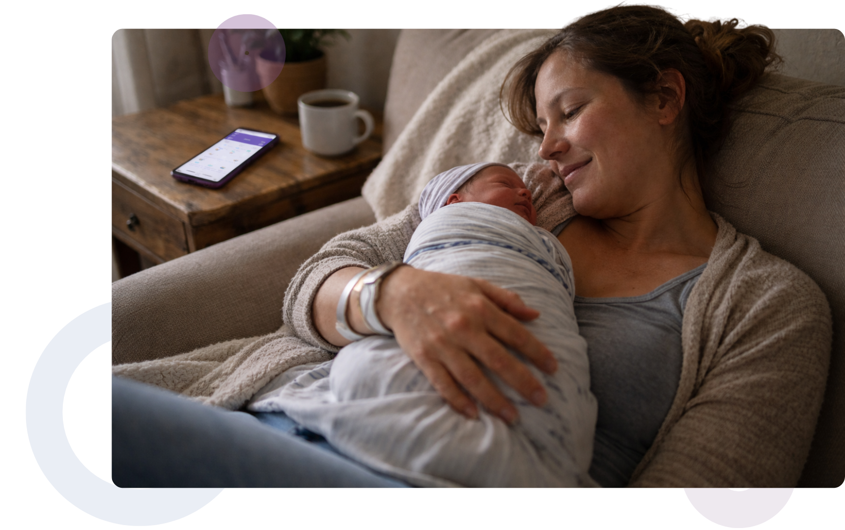 A new mother holding her baby, supported by a digital health app on her phone during early motherhood.