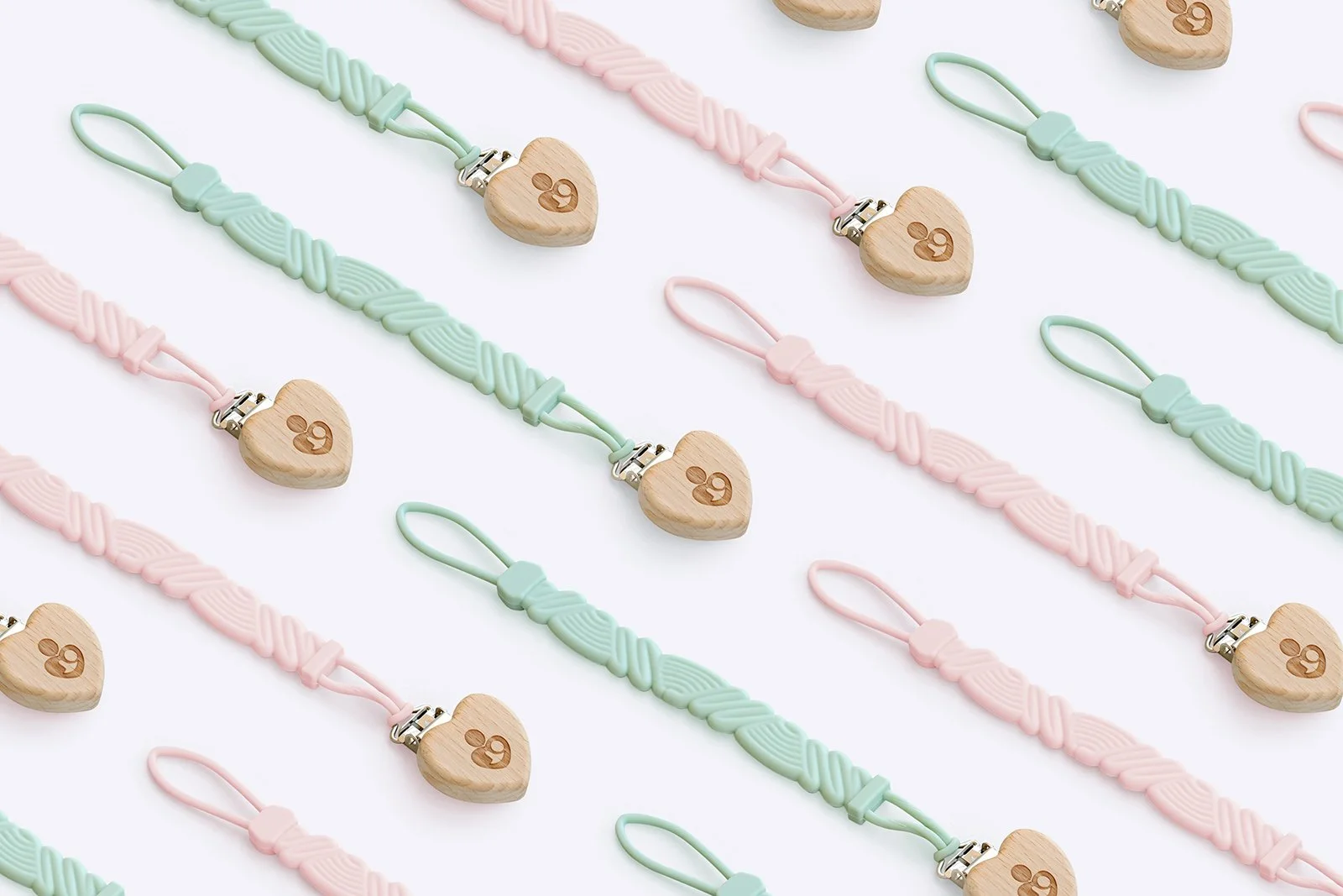 Pattern of pastel-colored silicone mask chains with wooden heart-shaped clips engraved with a small bear logo, arranged diagonally on a white background.