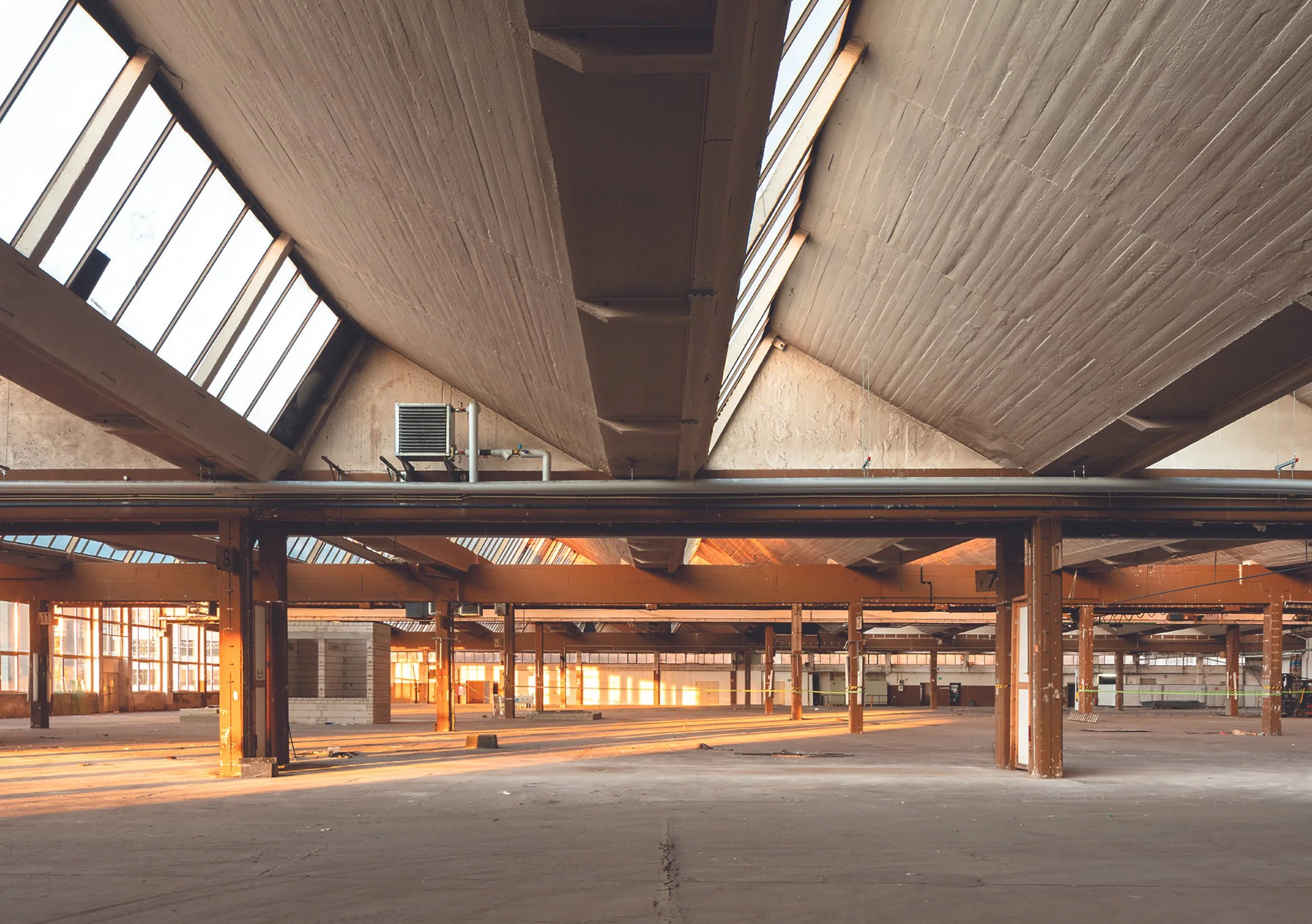 Leerer, verlassener Industrie- oder Lagerhalle mit hohen Decken, großen Fenstern und Sonnenlicht, das durch die Fenster fällt.