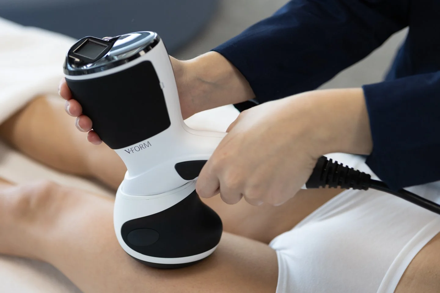 A person receiving a laser or light therapy treatment on their leg using a handheld medical device with the label V-FORM.