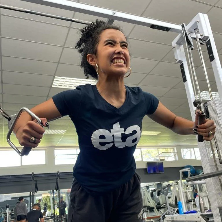 A woman at the gym pulling on a cable machine, showing a determined or intense facial expression.